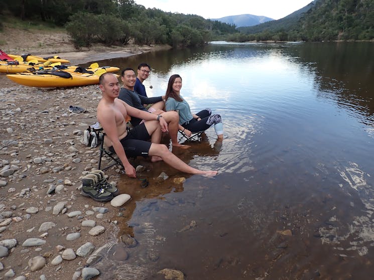 A group of people are sitting in the snowy river on chairs soaking there feet