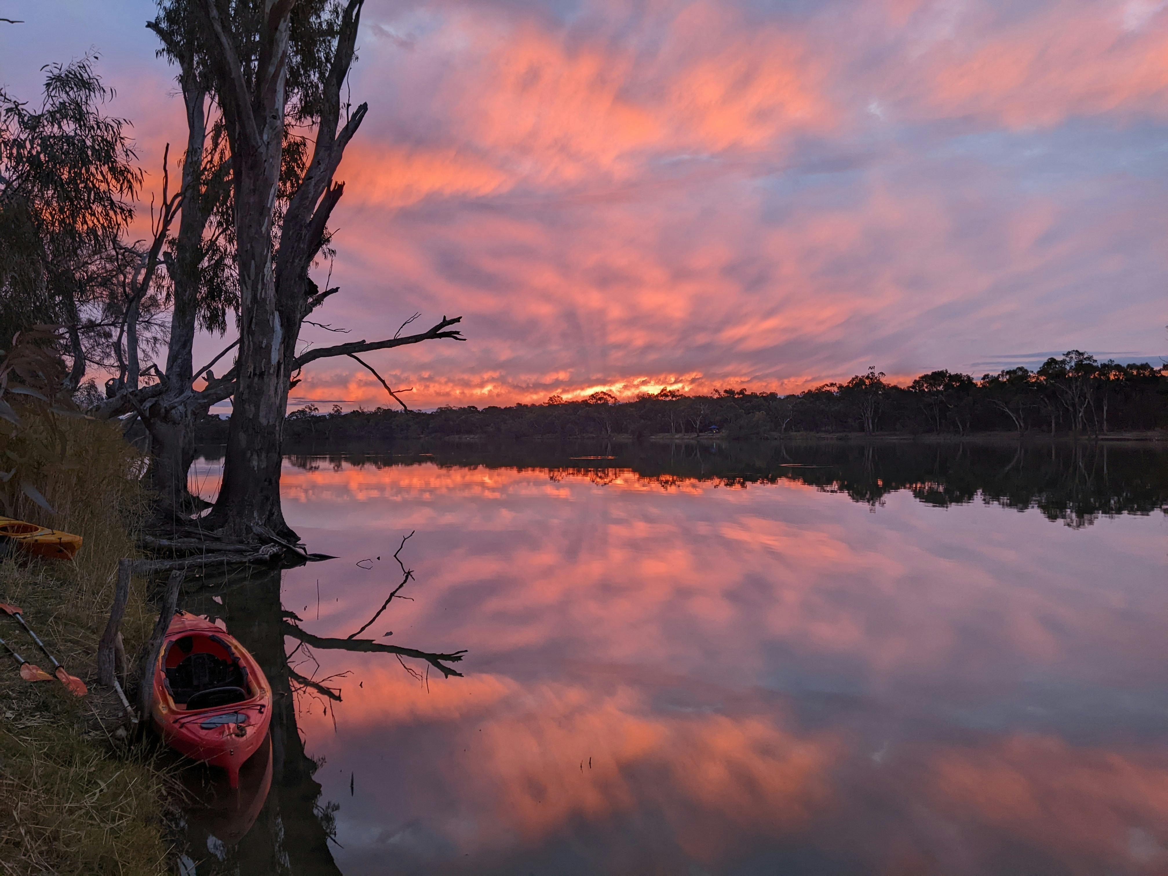 Kayak pulled up to the riverbank with beautiful pink sunset in the background