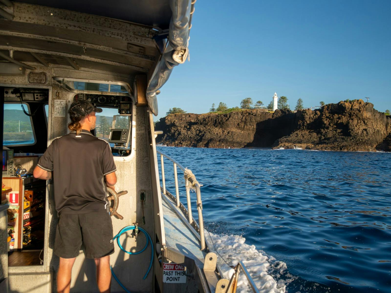 Man driving fishing charter boar standing holding steering wheel with his back to camera
