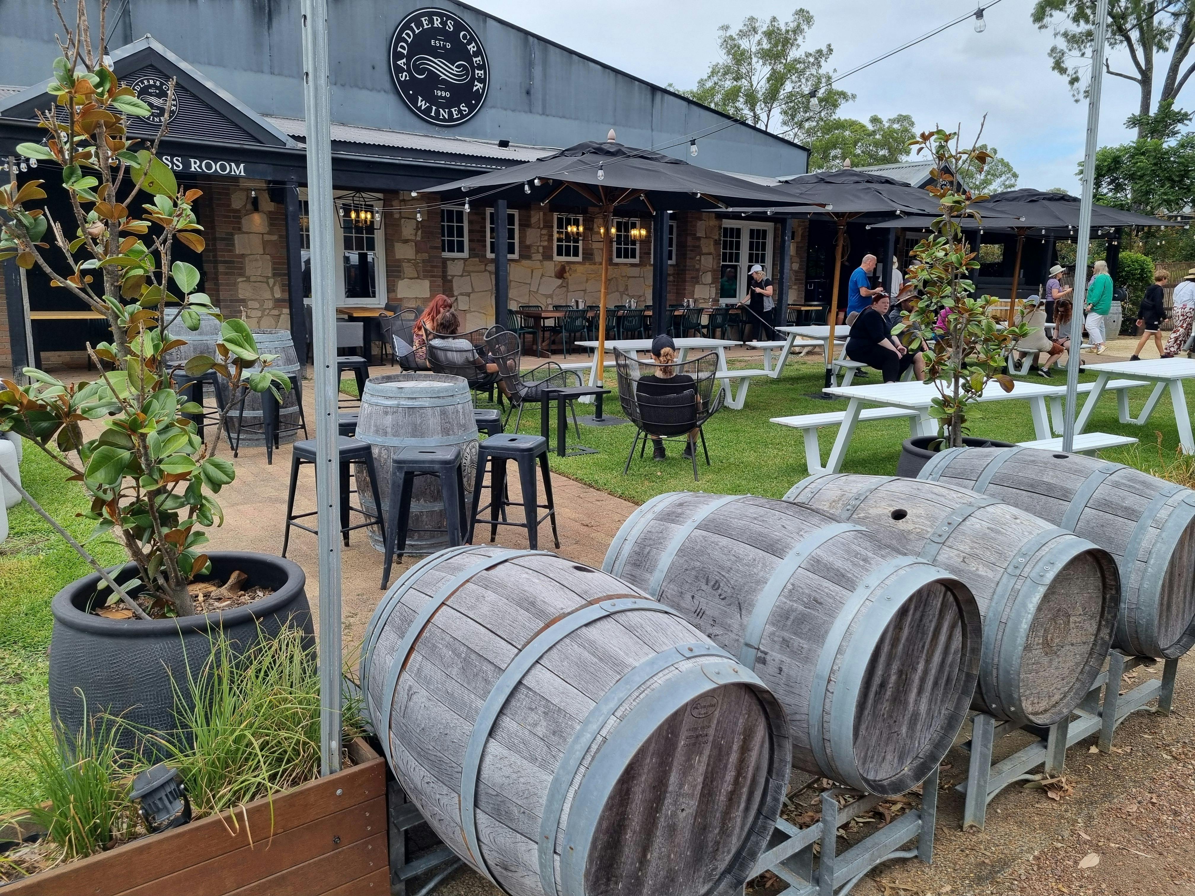 Weingarten im Freien am Saddler's Creek mit Weinfässern, Sitzbereichen und entspannenden Gästen