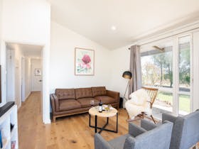 lounge room with brown lounge and grey chairs, a lamp and picture of a Waratah.