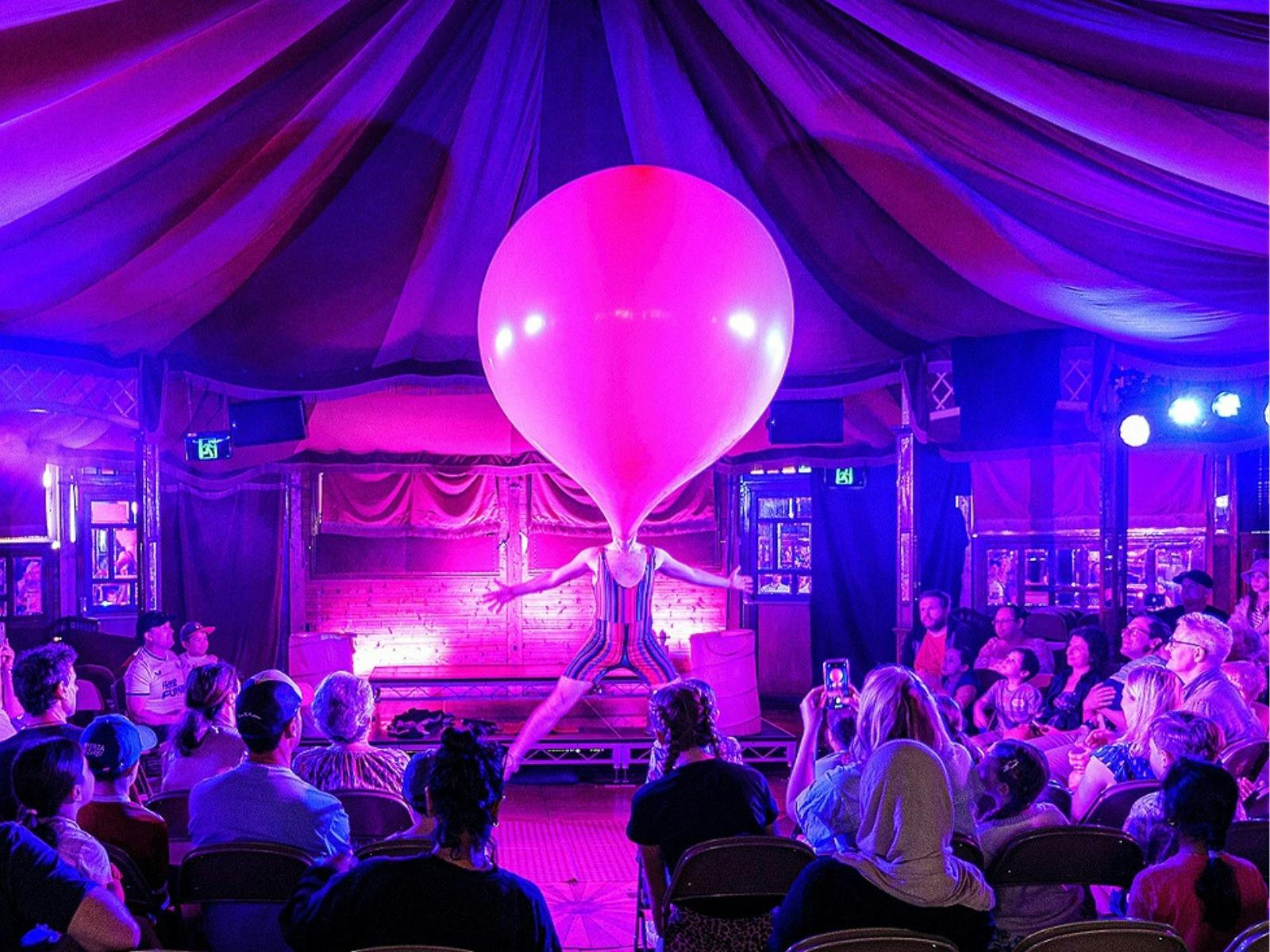 Man with a giant balloon over his head on stage in front of audience