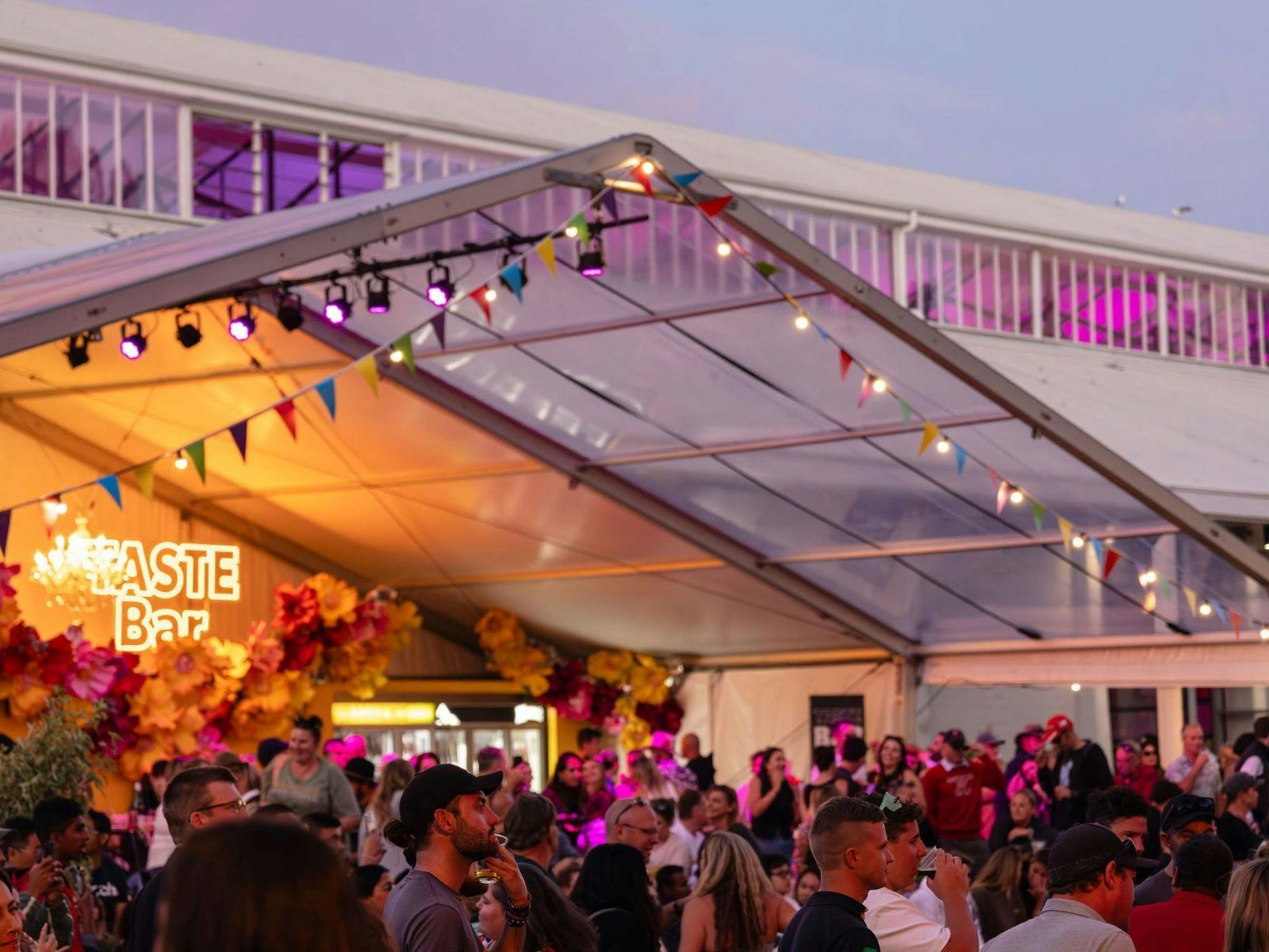 Festival-goers gather under a lit marquee decorated with flowers and colourful bunting.