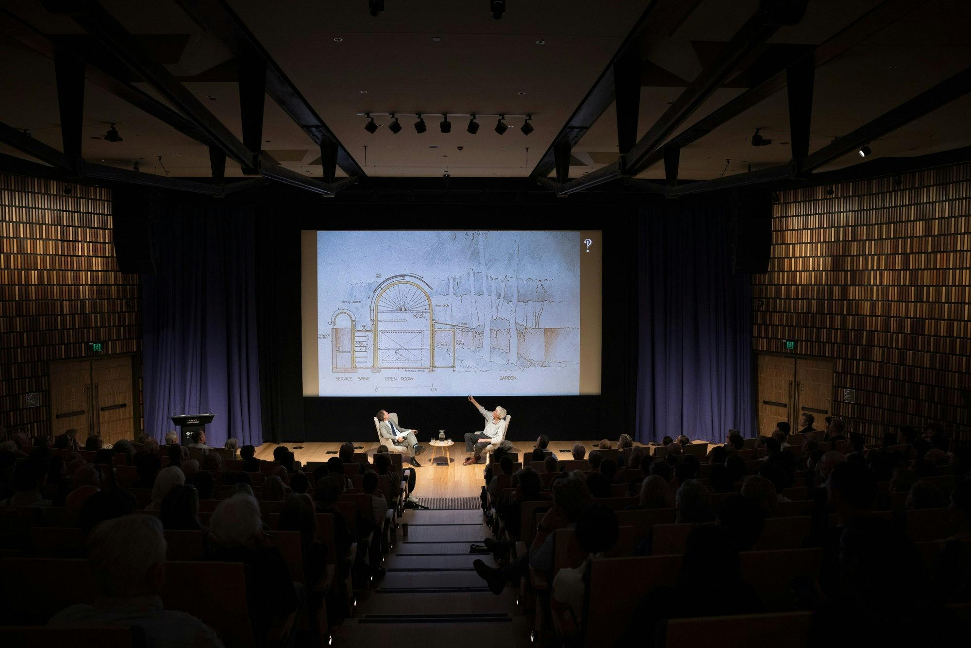 A full auditorium with a powerpoint slide on a  projector