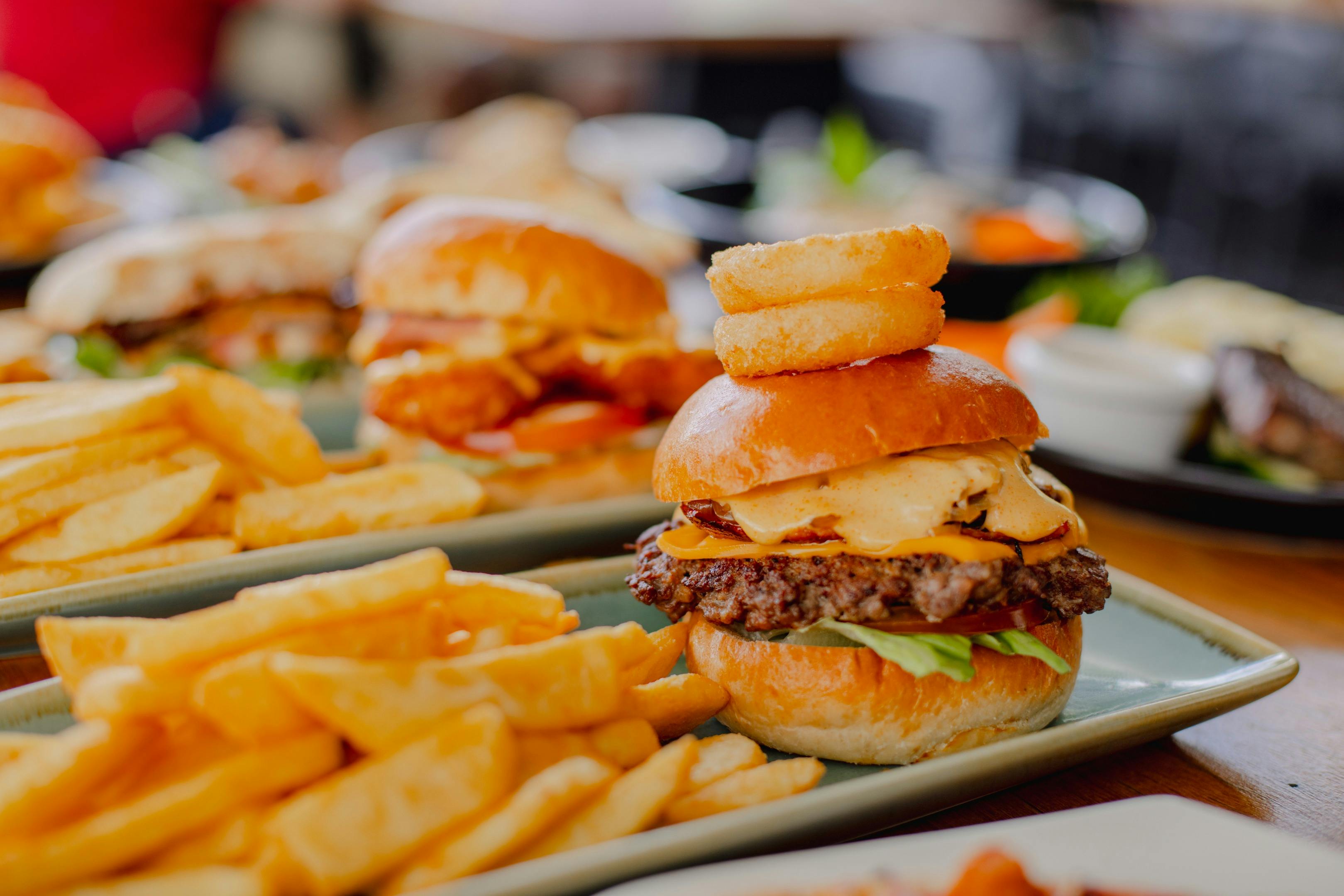 Two burgers on a plate with chips. A variety of food items in the background at Orion Hotel Ipswich