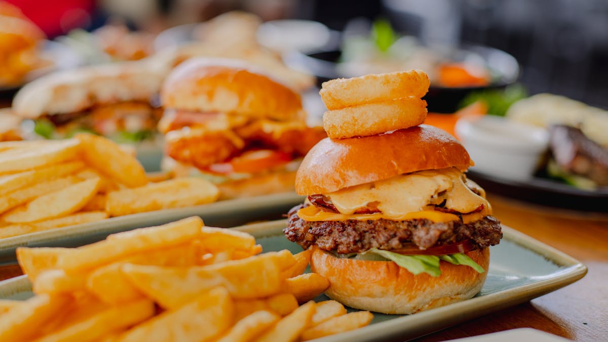 Two burgers on a plate with chips. A variety of food items in the background at Orion Hotel Ipswich