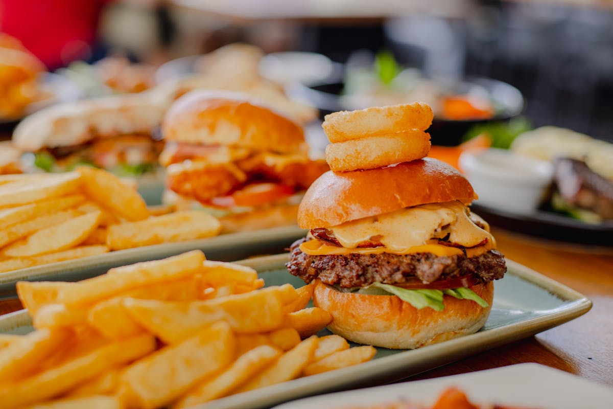 Two burgers on a plate with chips. A variety of food items in the background at Orion Hotel Ipswich