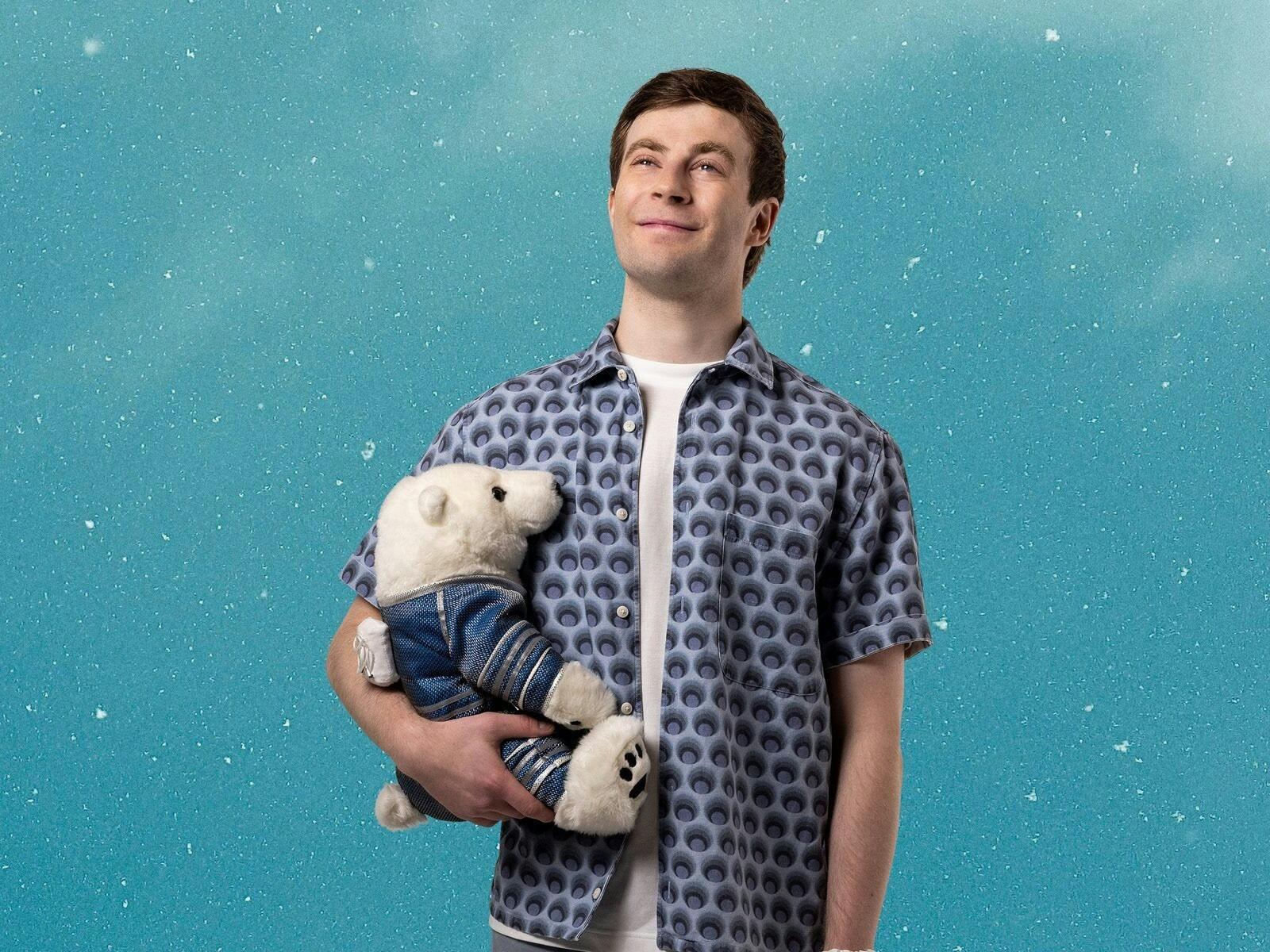 Young man dressed in open blue shirt and white tshirt, holding a toy white bear