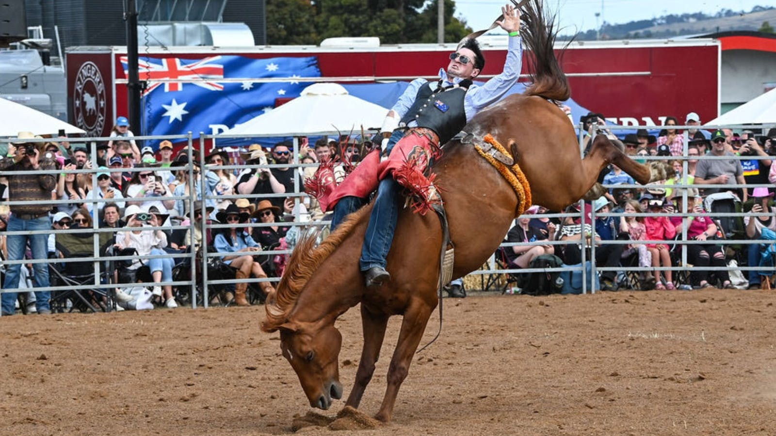 A cowboy lays horizontal on a bareback bronc in front of a sold out crowd