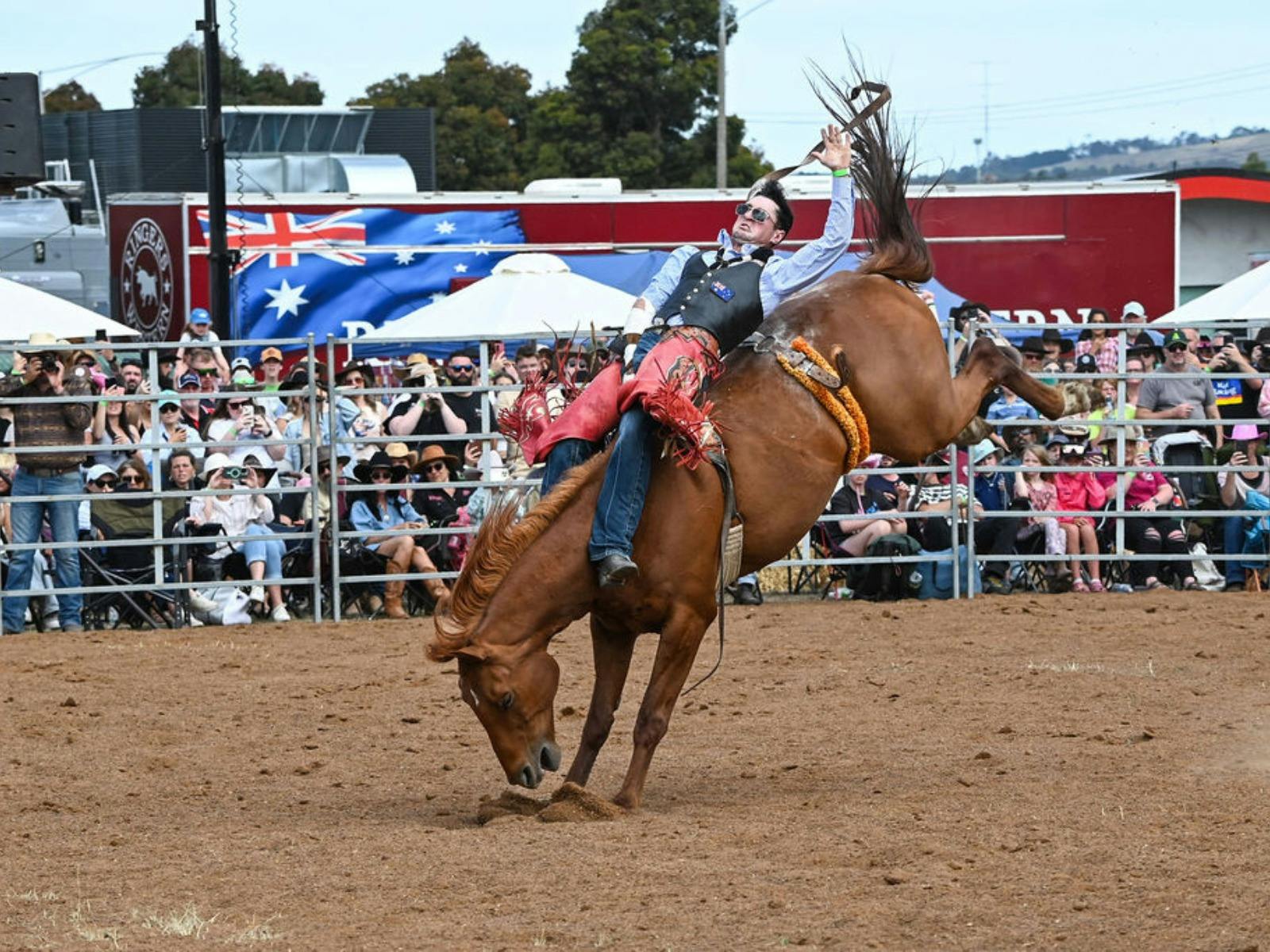 A cowboy lays horizontal on a bareback bronc in front of a sold out crowd