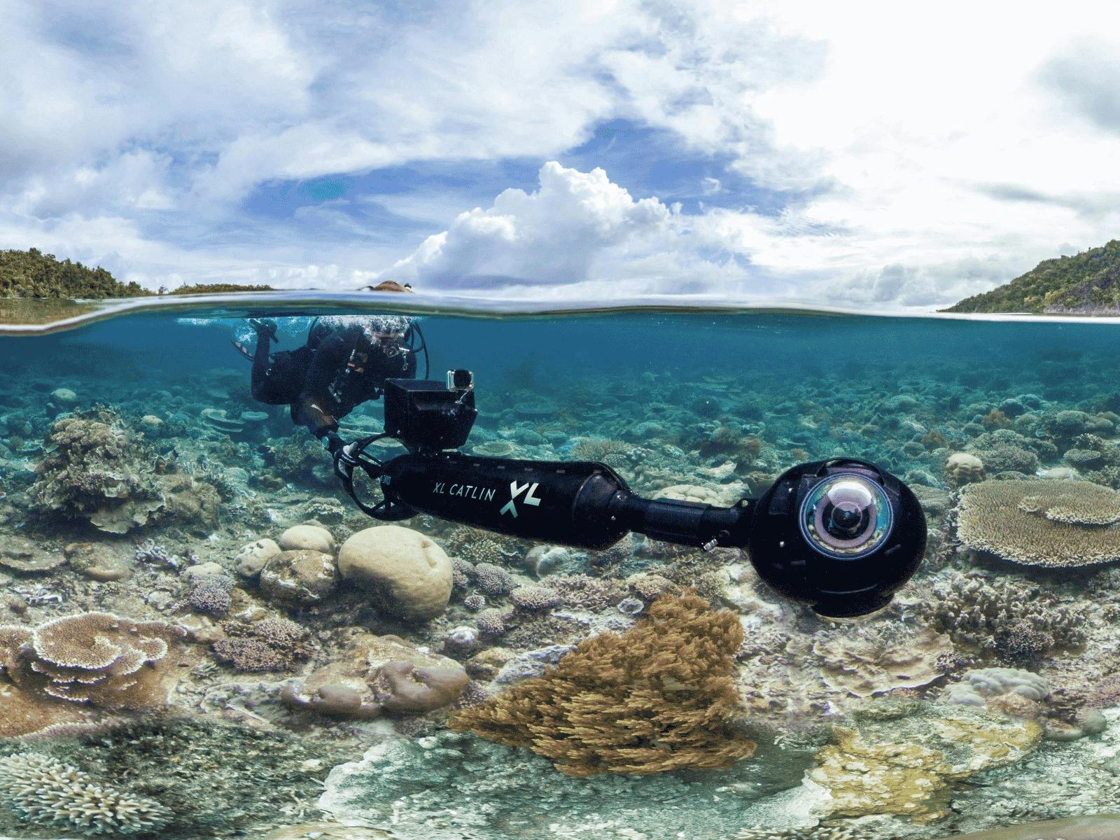 A scuba diver holds a strange, futuristic camera over a coral reef