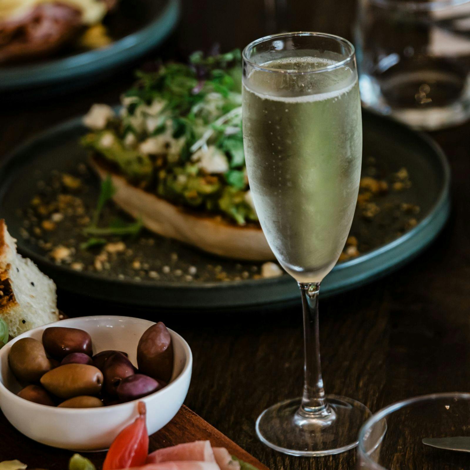 A glass of Champagne sits surrounded by plates of food