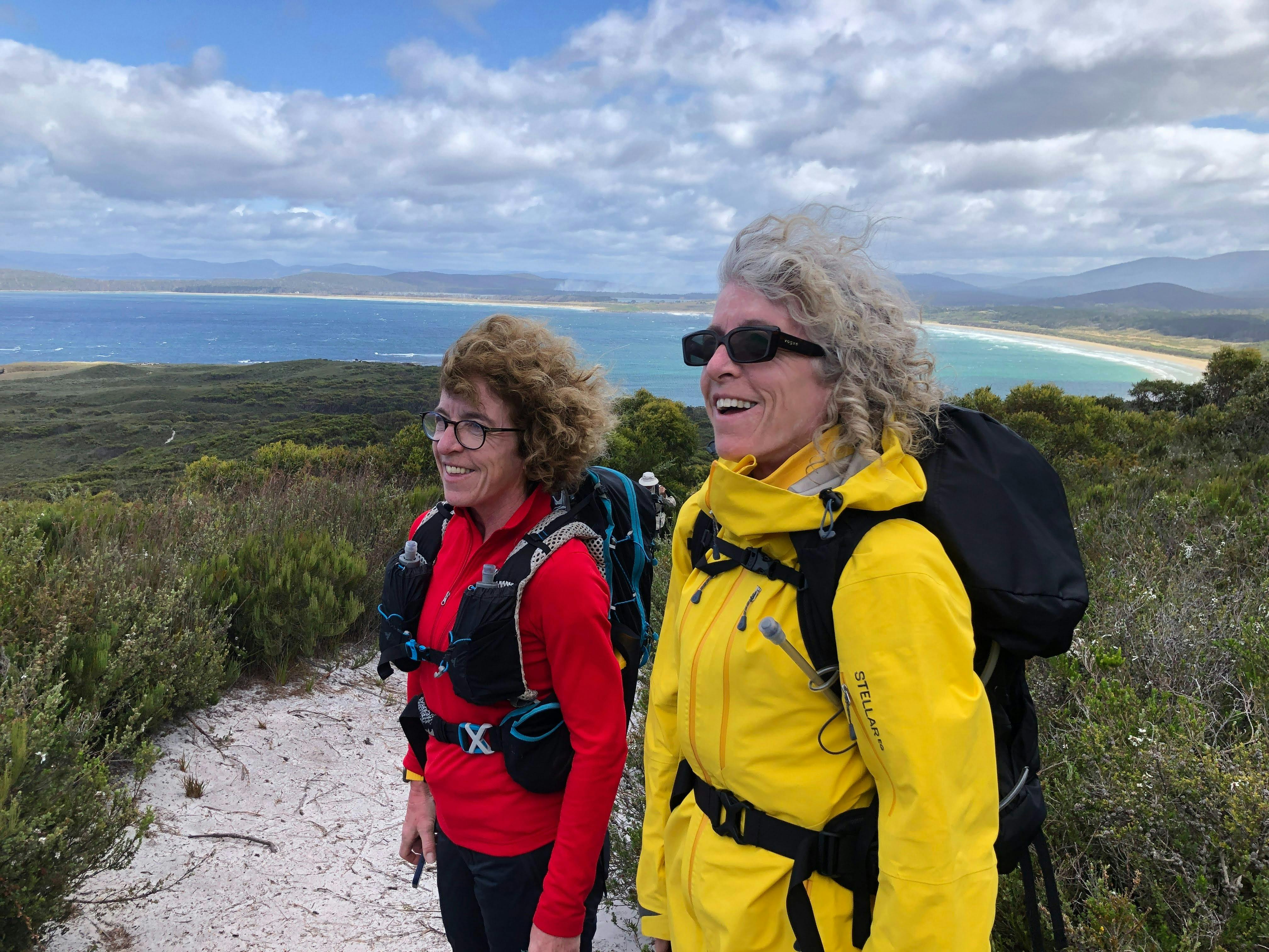 Two hikers with backpacks looking over coastline views on a Bruny Island walking tour in Tasmania.