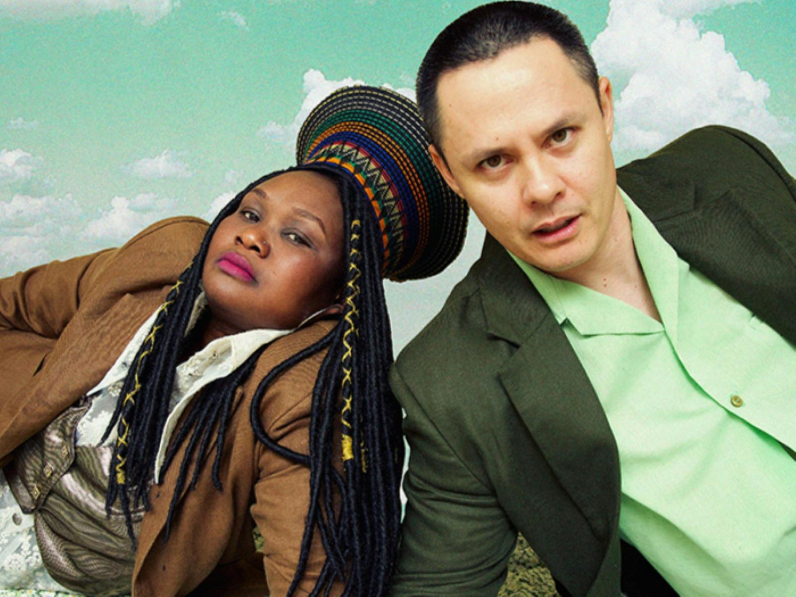 Awoman in a woven hat and brown jacket reclines beside a man in a green shirt.