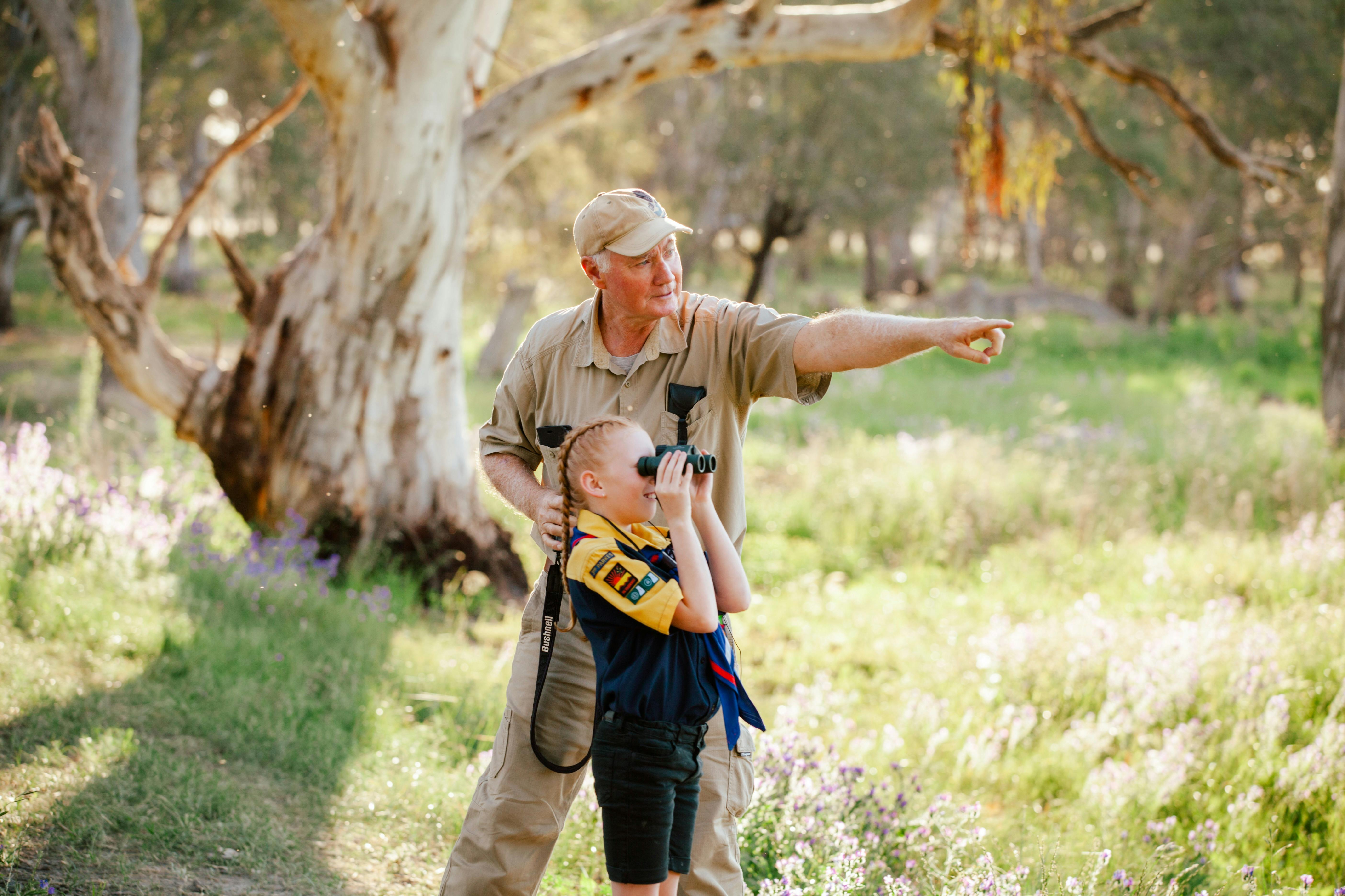 Elderly gentleman pointing and young girl looking through binoculars