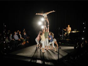 5 acrobats hold another acrobat in the air and upsideown