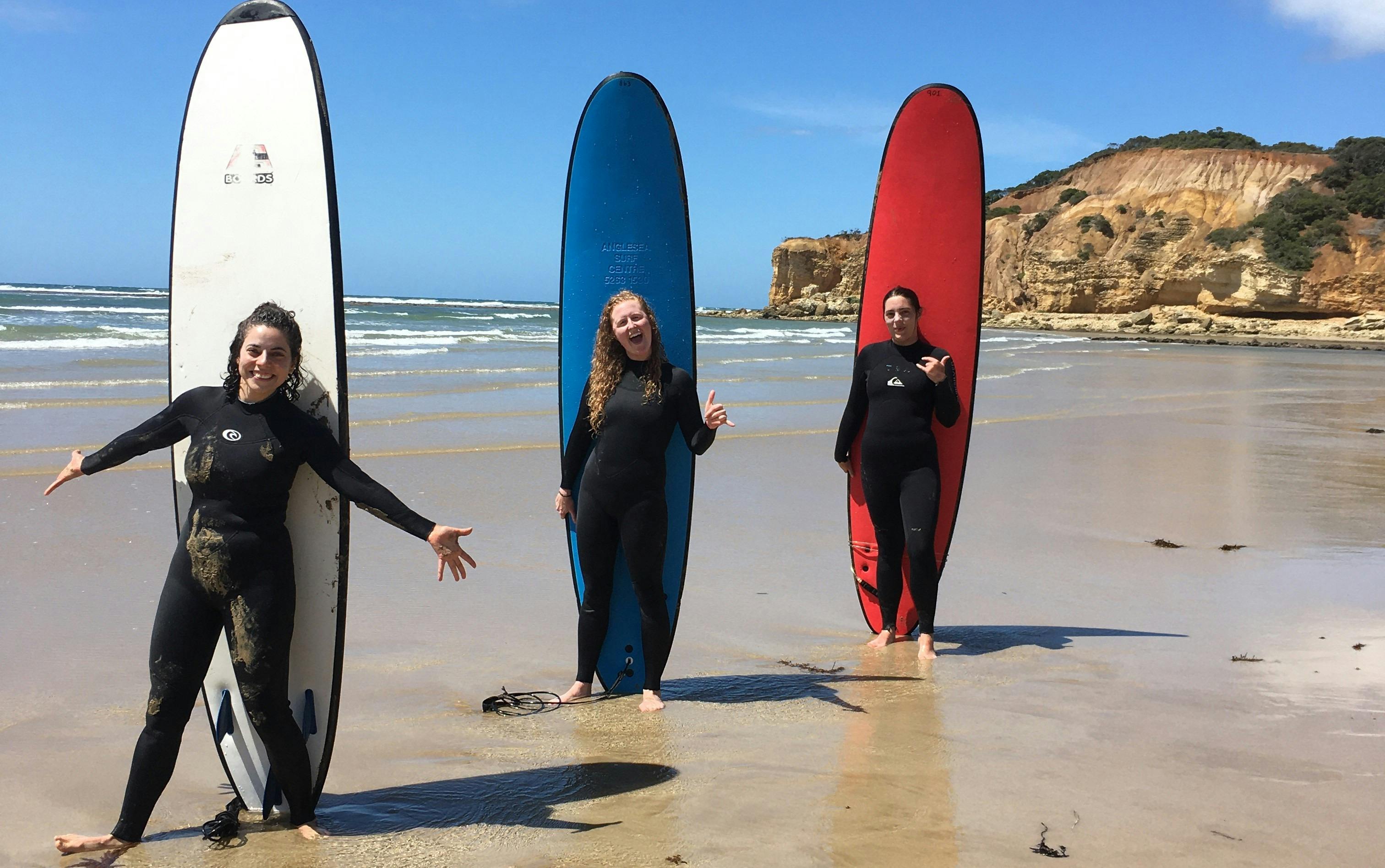 Three surfers standing with boards behind them smiling with the ocean rolling in behind them.