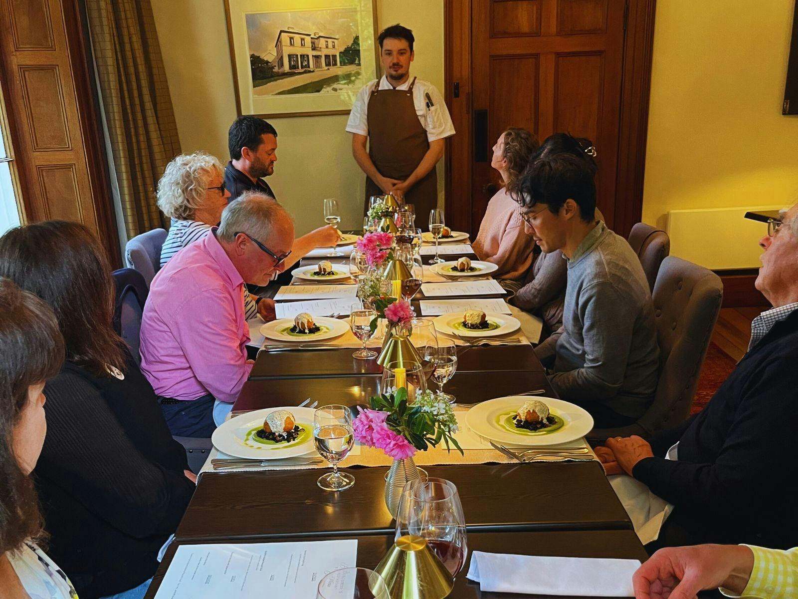 A group of people at a tabels with food and the chef explaining the food