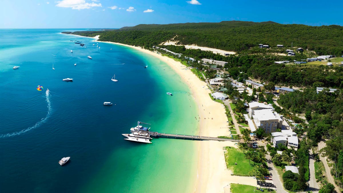 Boat at a jetty and a resort situated on a sandy beach and turquoise water