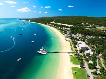 Boat at a jetty and a resort situated on a sandy beach and turquoise water