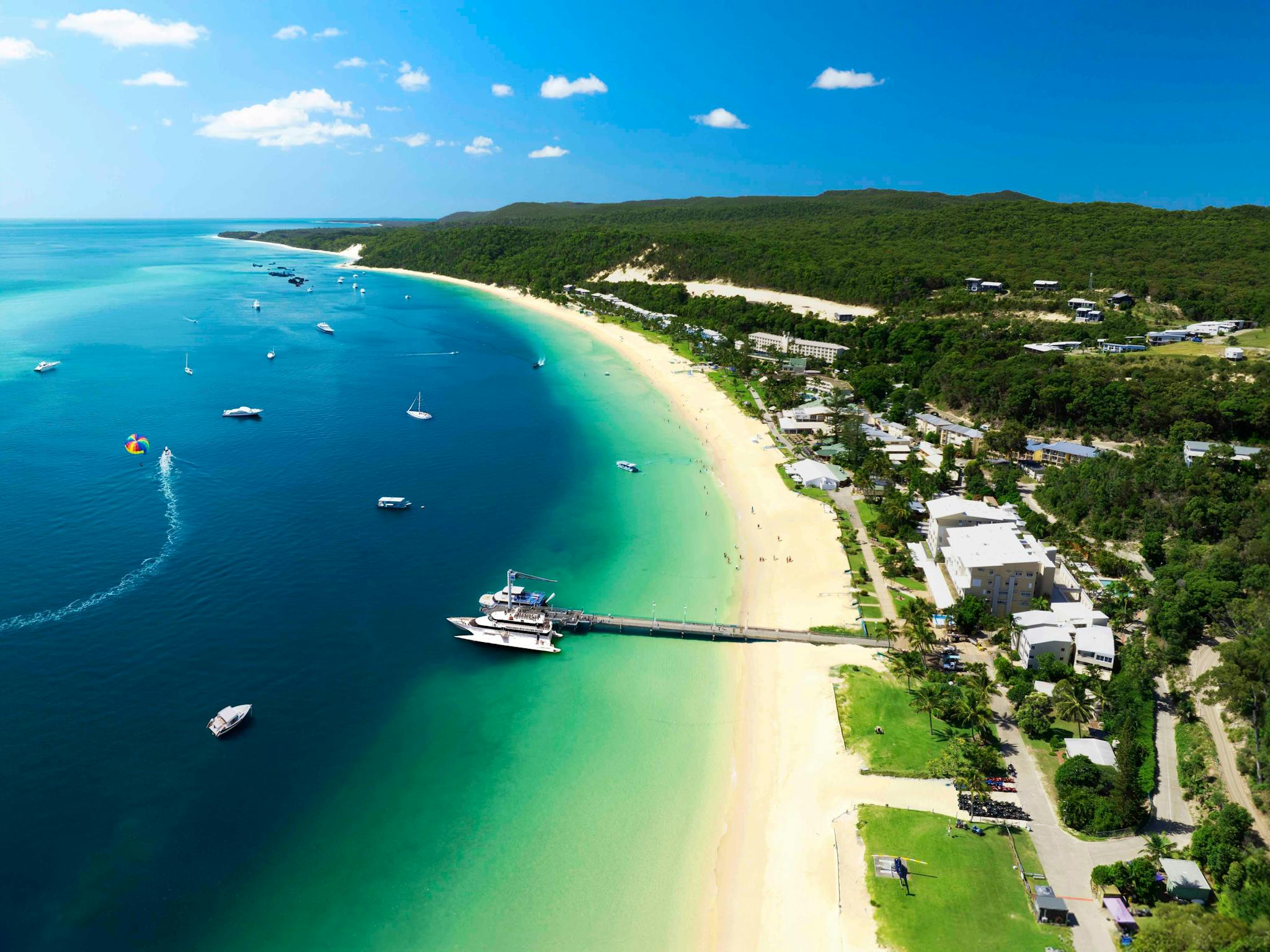 Boat at a jetty and a resort situated on a sandy beach and turquoise water Boat at a jetty and a resort situated on a sandy beach and turquoise water