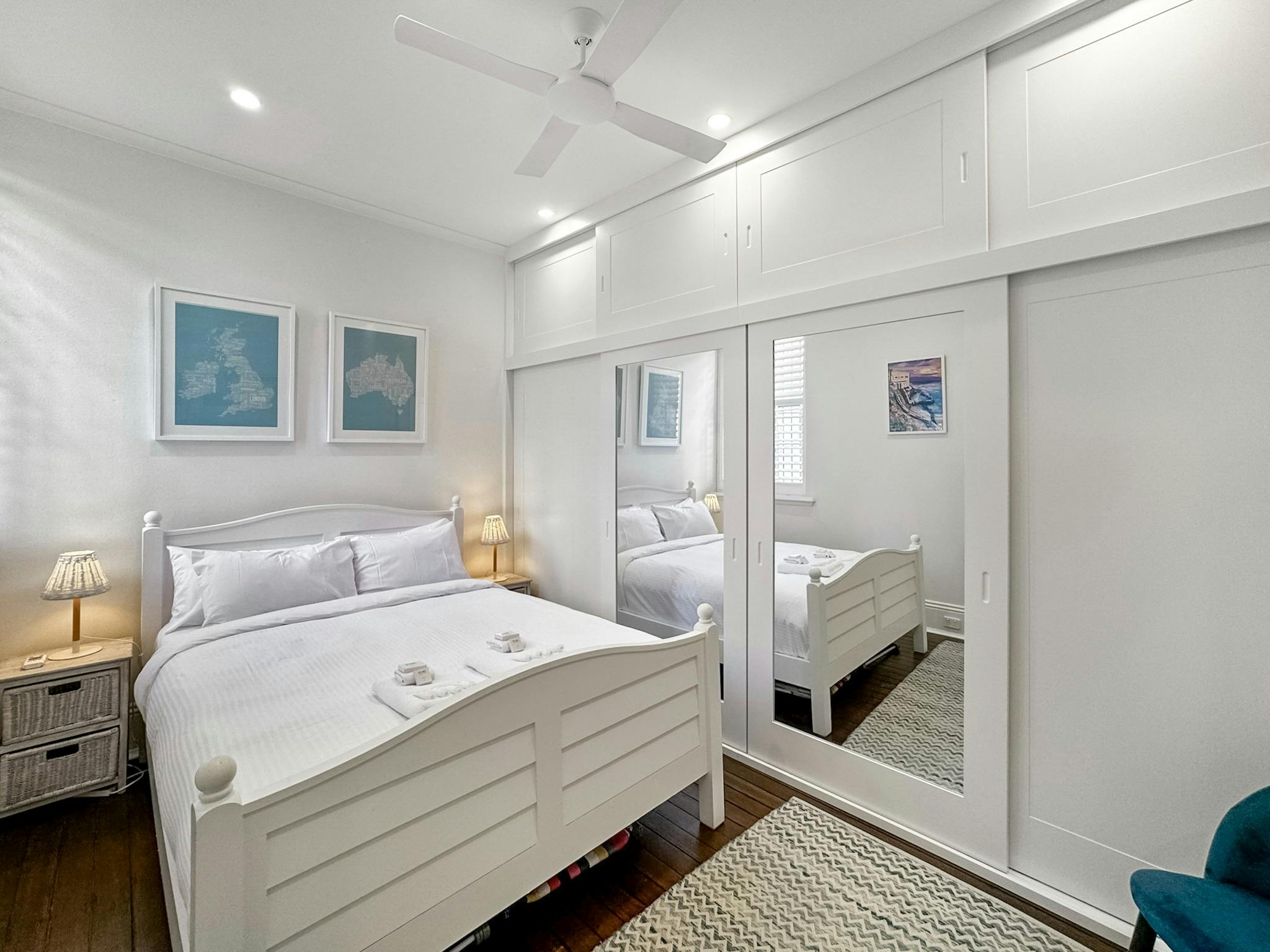 臥室配有白色床、裱框地圖和反映空間的鏡面衣櫃。