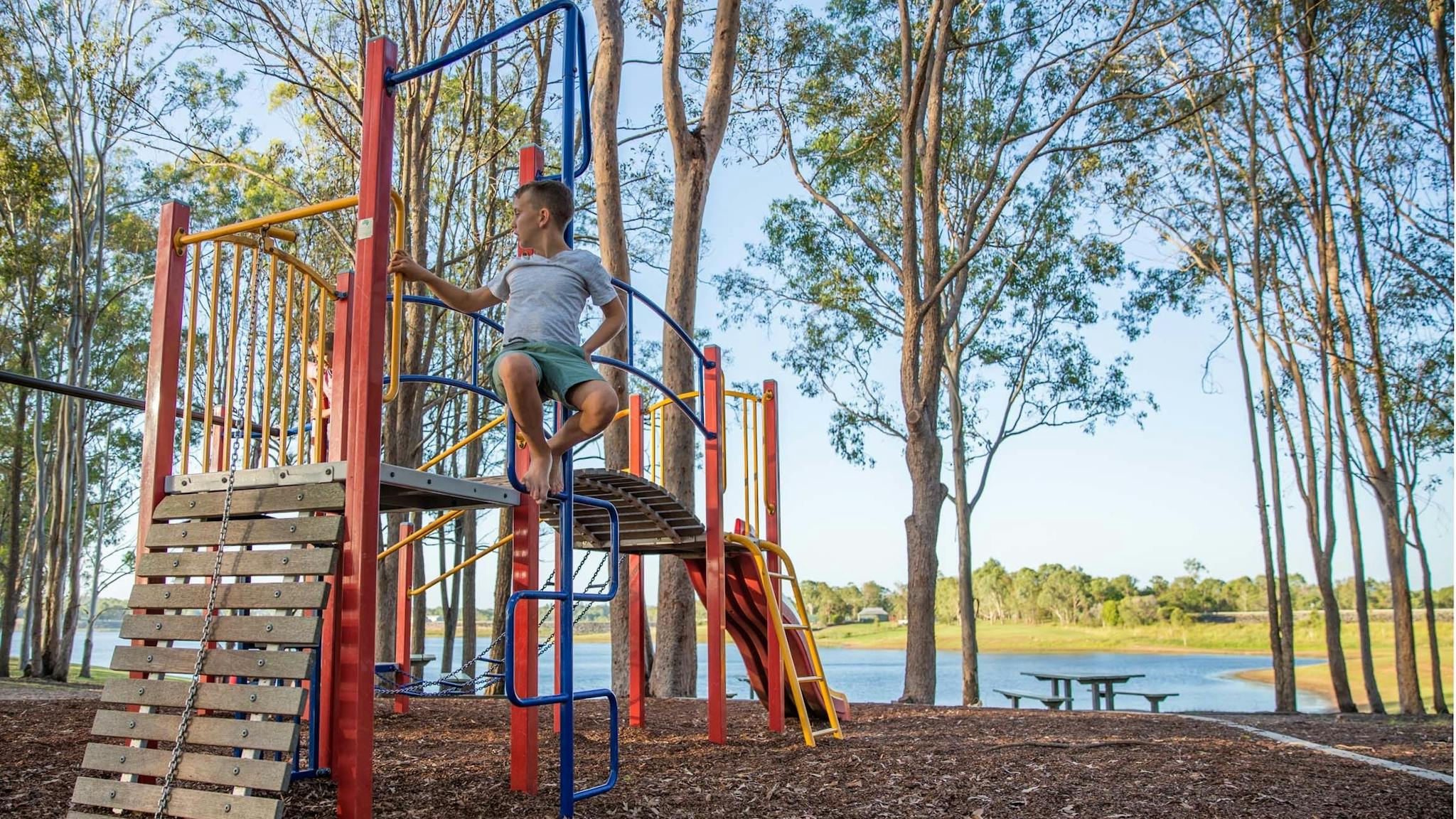 Male child sitting on colourful children's playground beside a lake