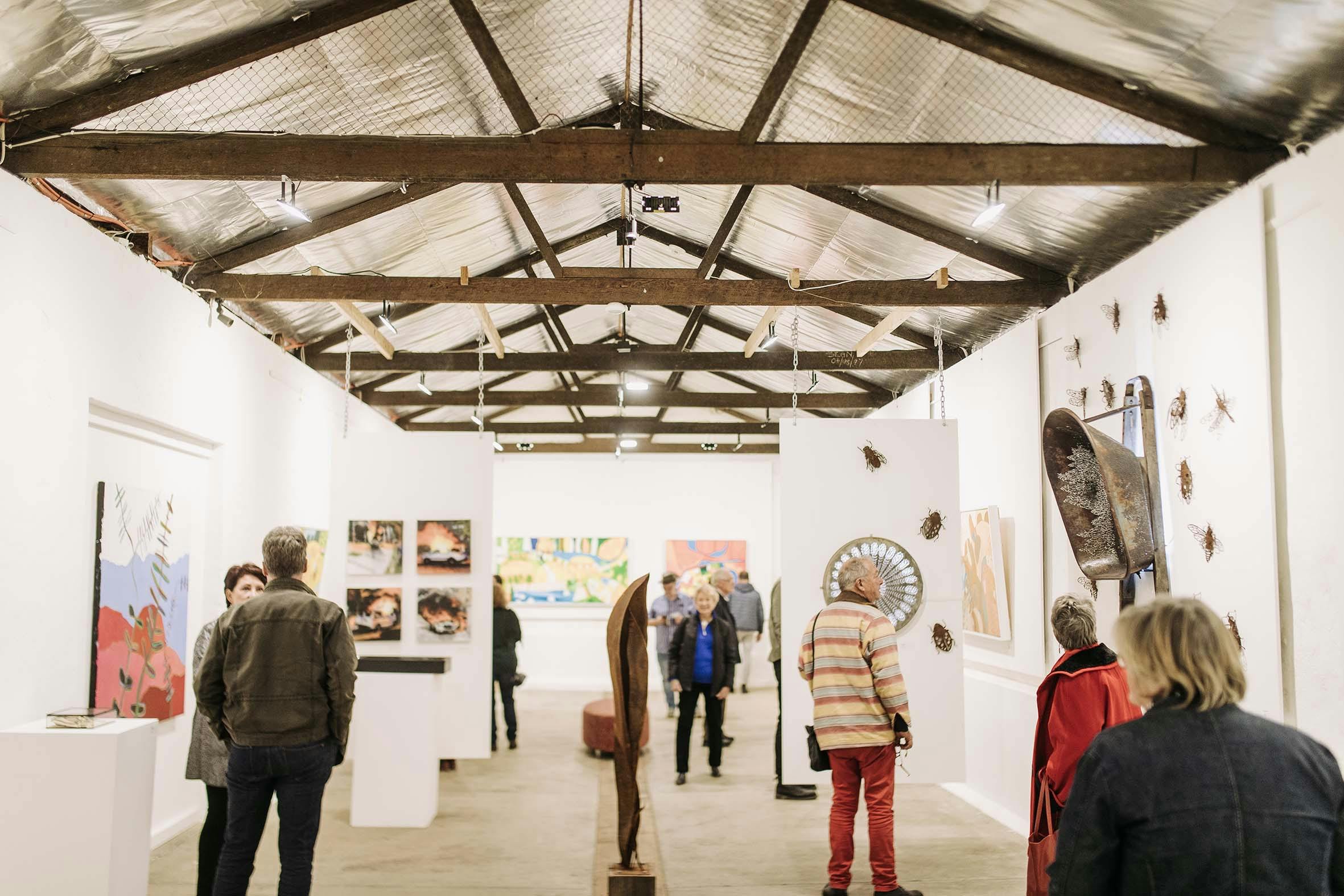 this is a photo of a large gallery with people looking at paintings at sculptures