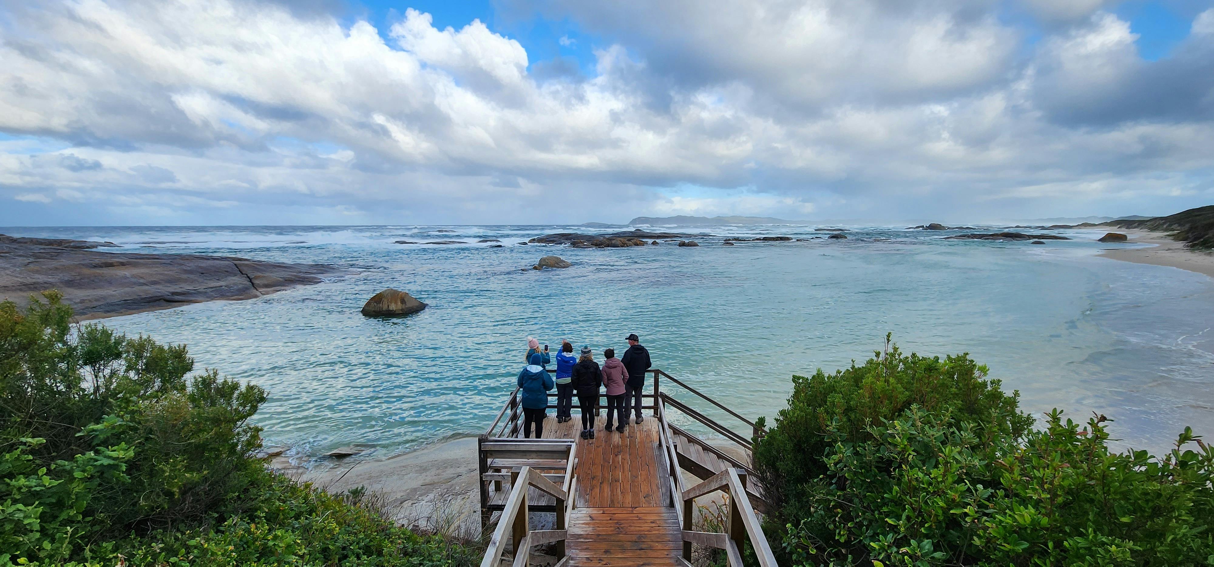 Hikers standing on boardwalk with beautiful blue calm ocean in background