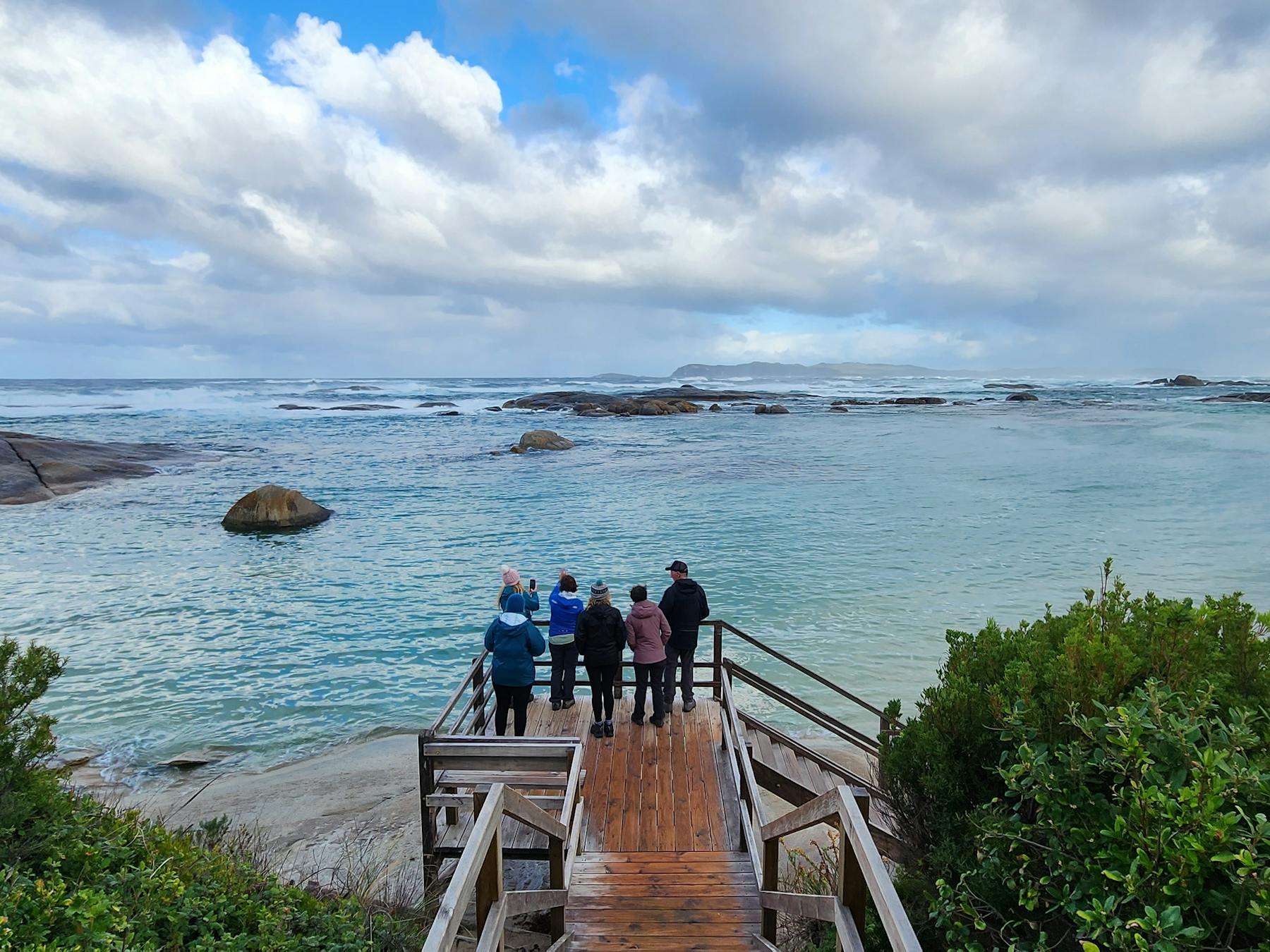 Hikers standing on boardwalk with beautiful blue calm ocean in background