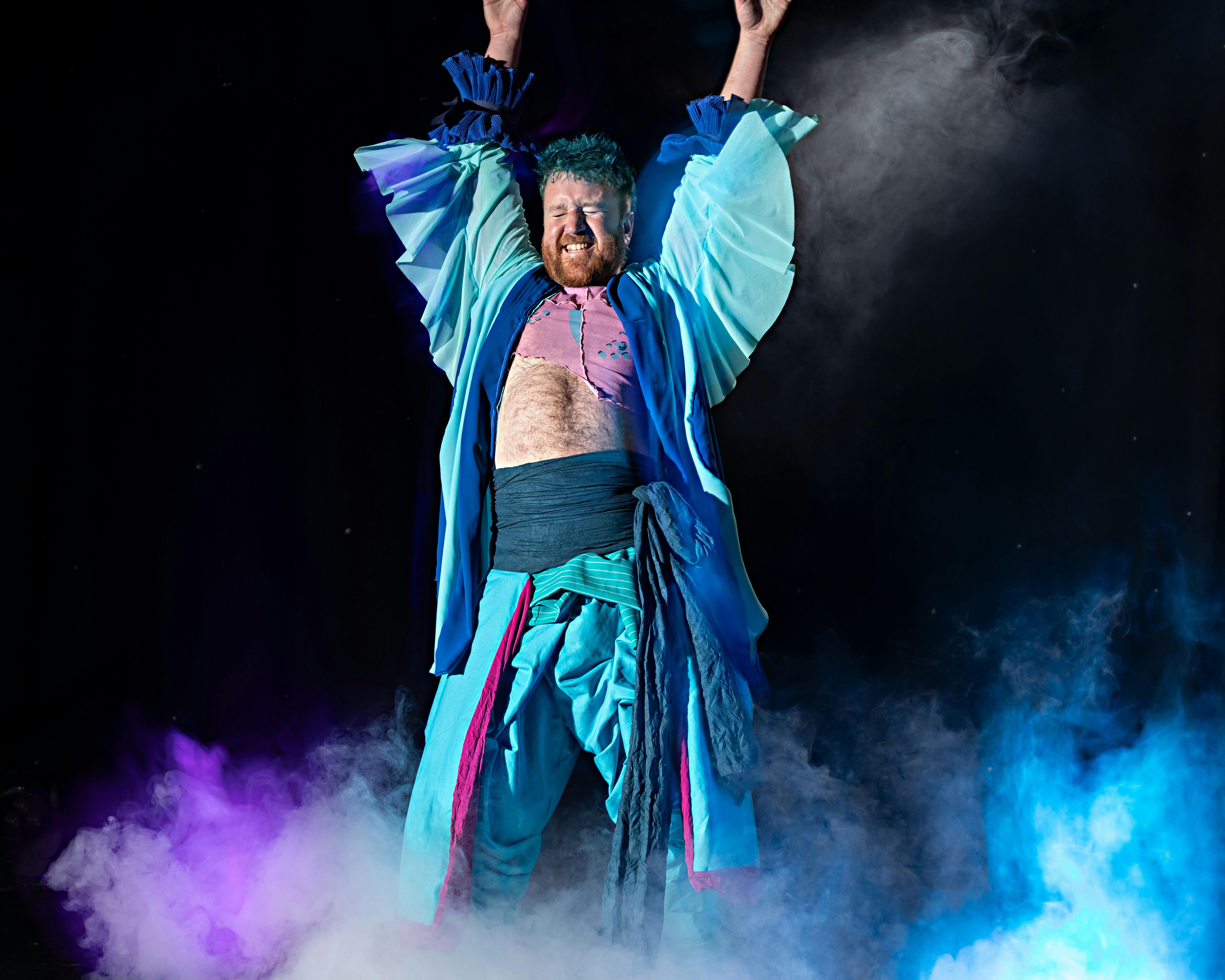 A man is dressed in a blue coat and has his hands raised in glee.