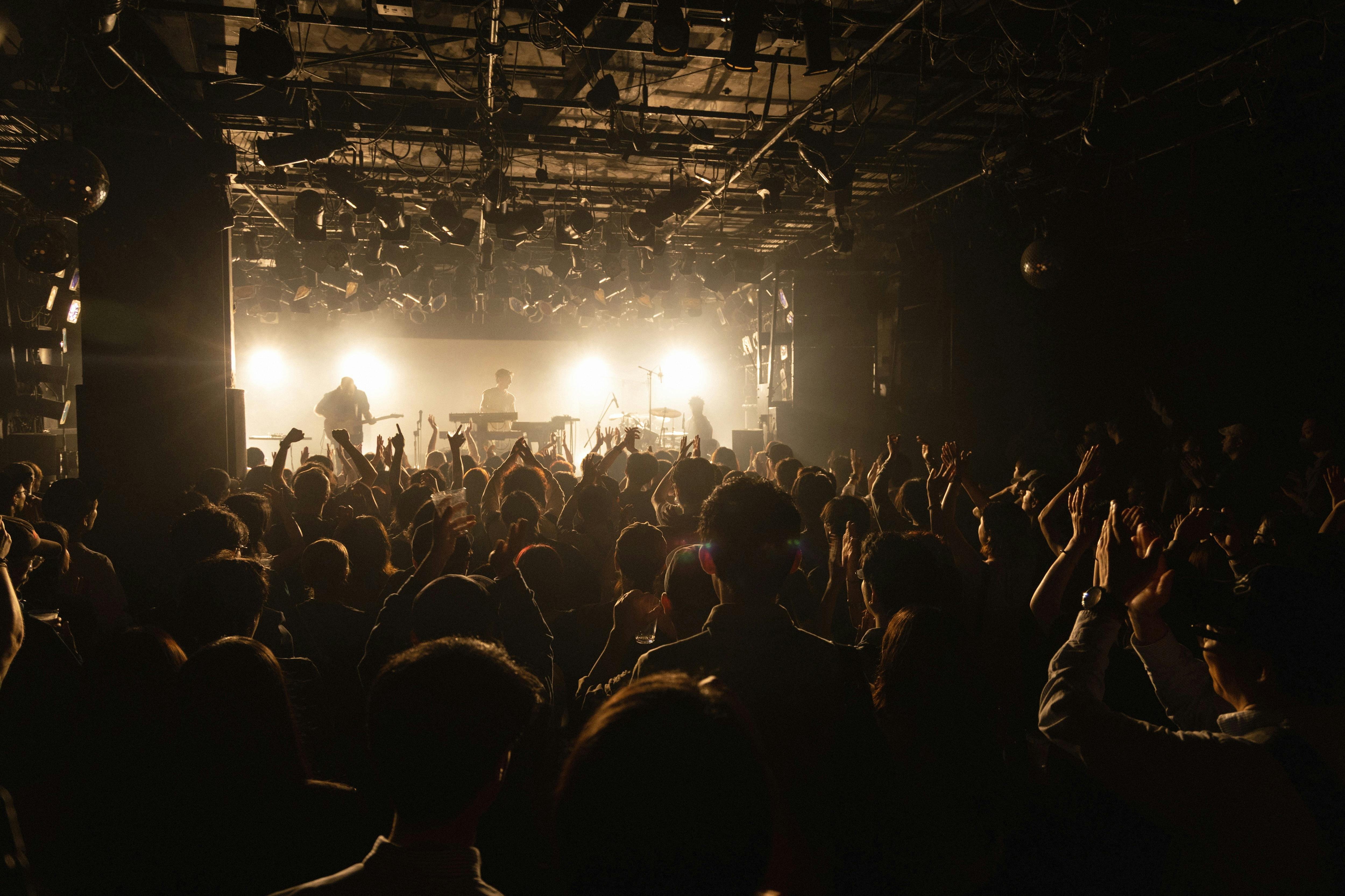 Image taken from the back of a big crowd watching a performance on stage with bright lights.