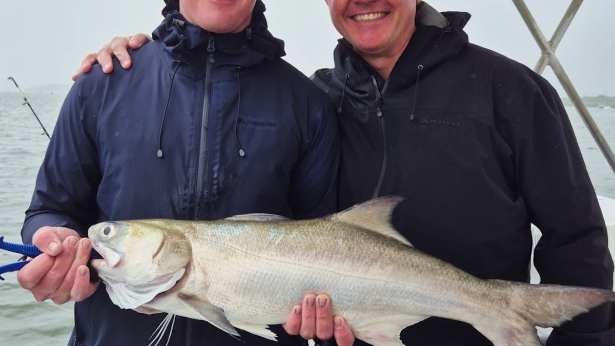 Men holding salmon catch with Gone Fishing Cairns on the calm Trinity Inlet