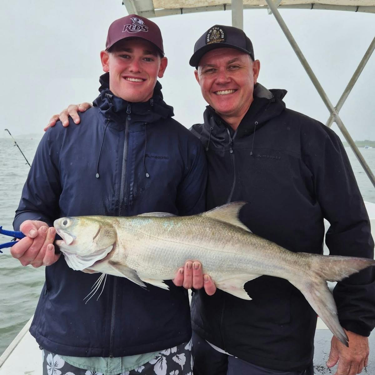 Men holding salmon catch with Gone Fishing Cairns on the calm Trinity Inlet