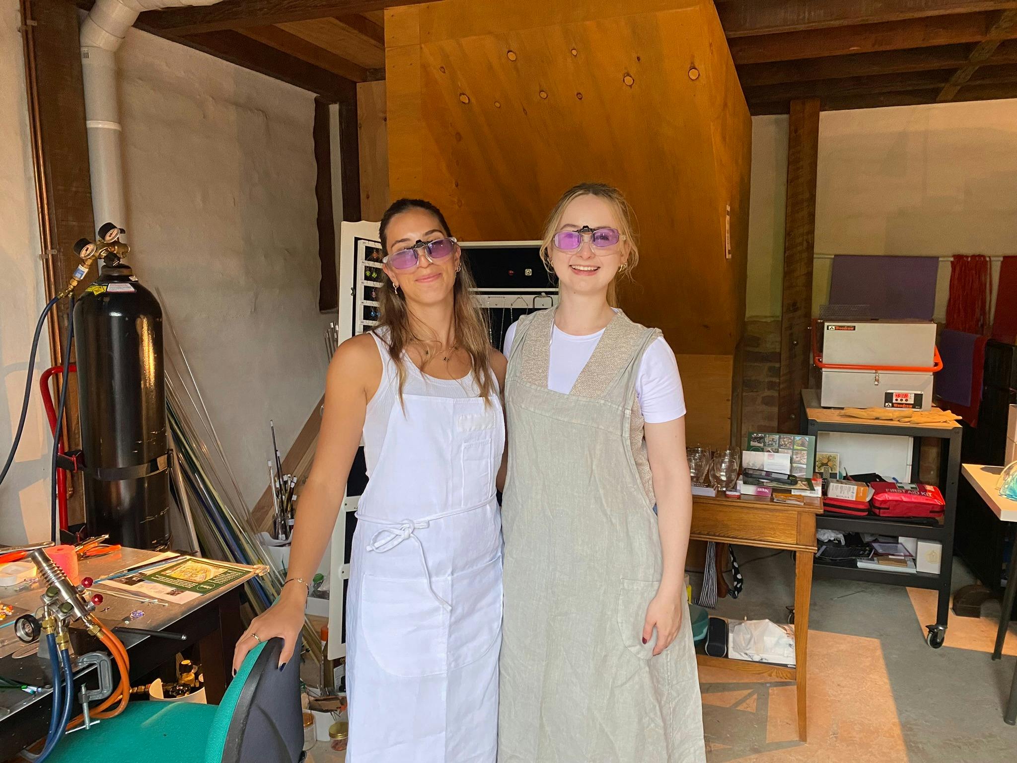 two women standing side by side at a glass workshop