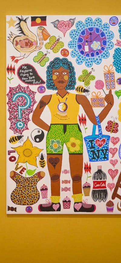 Two young people view a portrait, and in the foreground, a colourful portrait hangs on a yellow wall