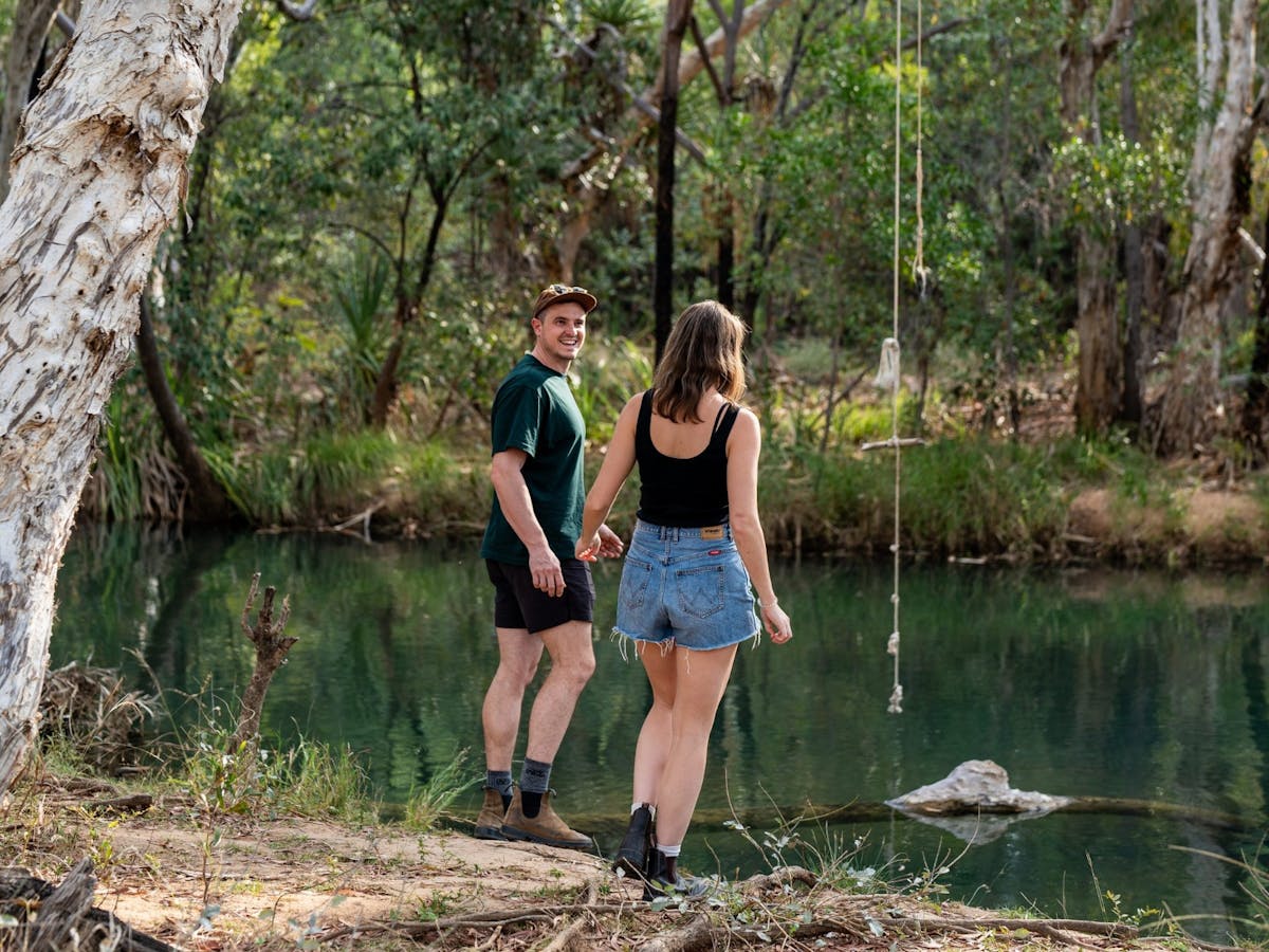 Man and woman walk by the waters edge at the Walsh River Weir in Chillagoe, North Qld.