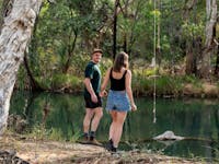 Man and woman walk by the waters edge at the Walsh River Weir in Chillagoe, North Qld.