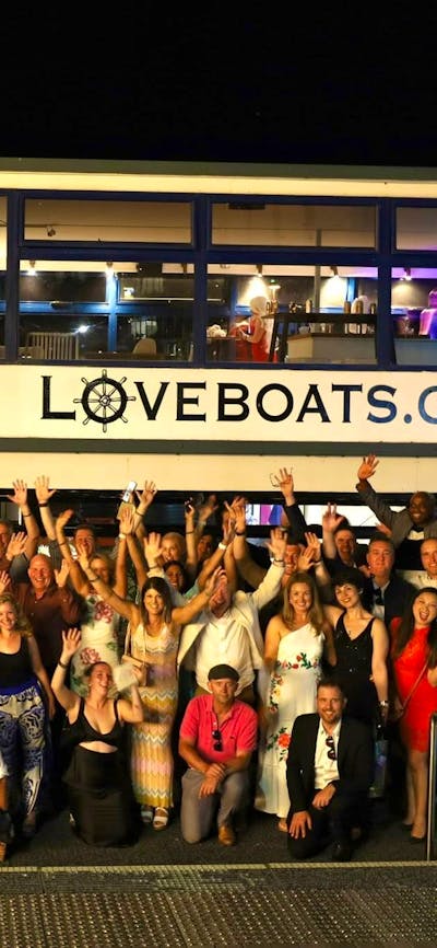 Group of people standing alongside Love Boat having a party