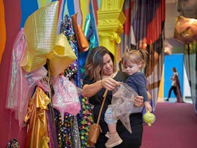 Mother and toddler look at glittering costumes in a brightly painted gallery