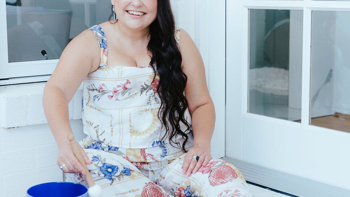 Founder of Harmonic Sanctum Sandy sitting on the ground with a blue crystal singing bowl