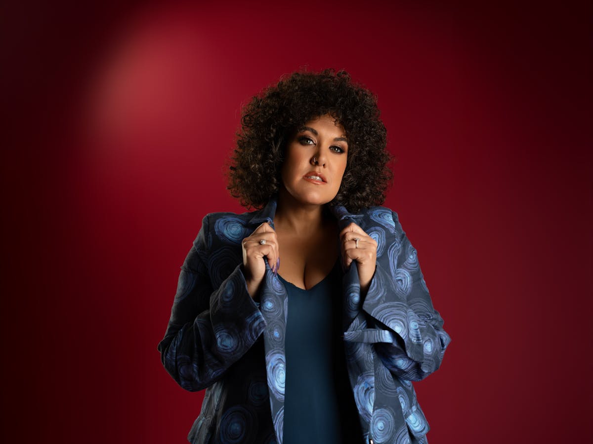 Casey with curly hair and hands on collar of shirt