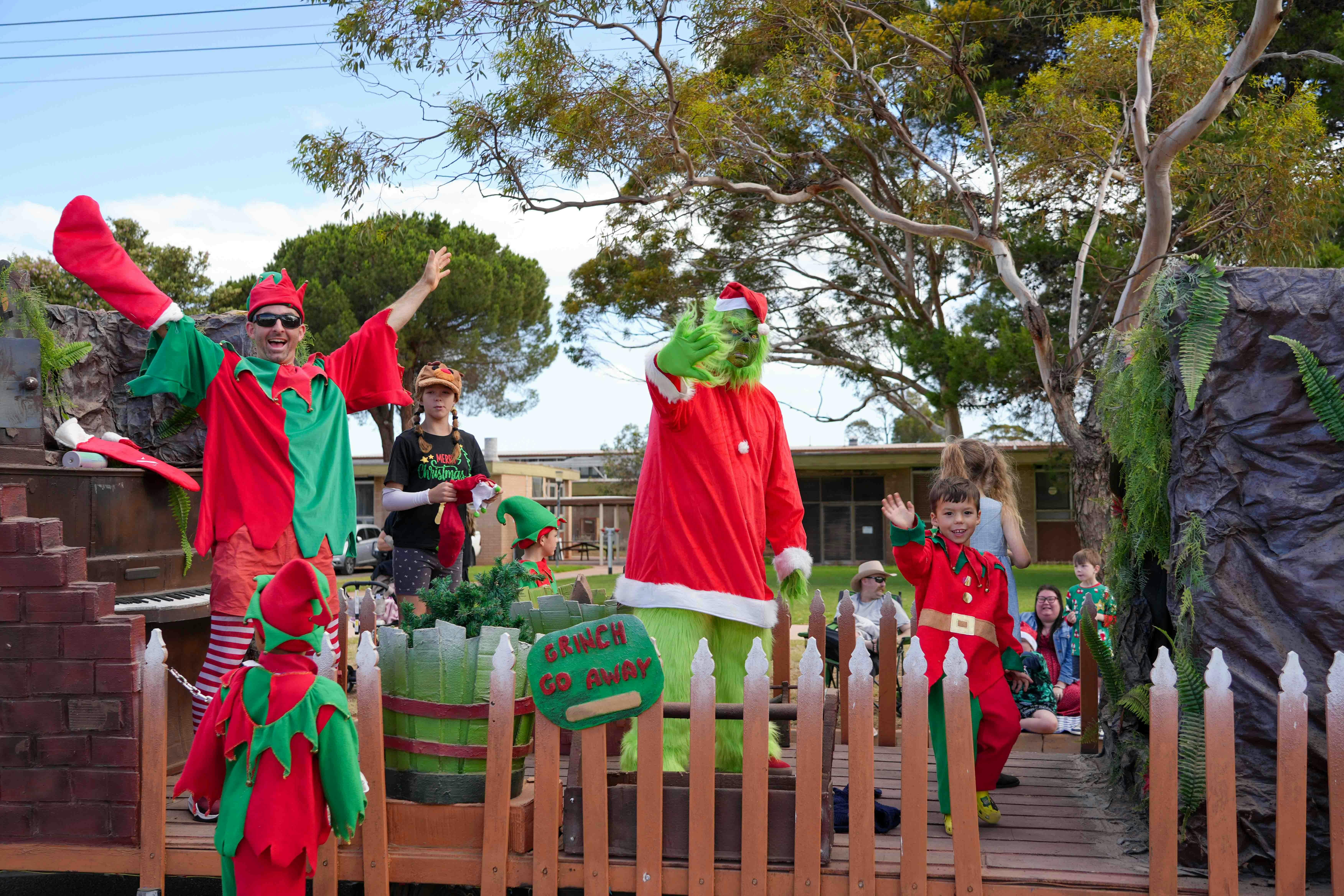 The green grinch standing on the grinch workshop float with other elves  waving