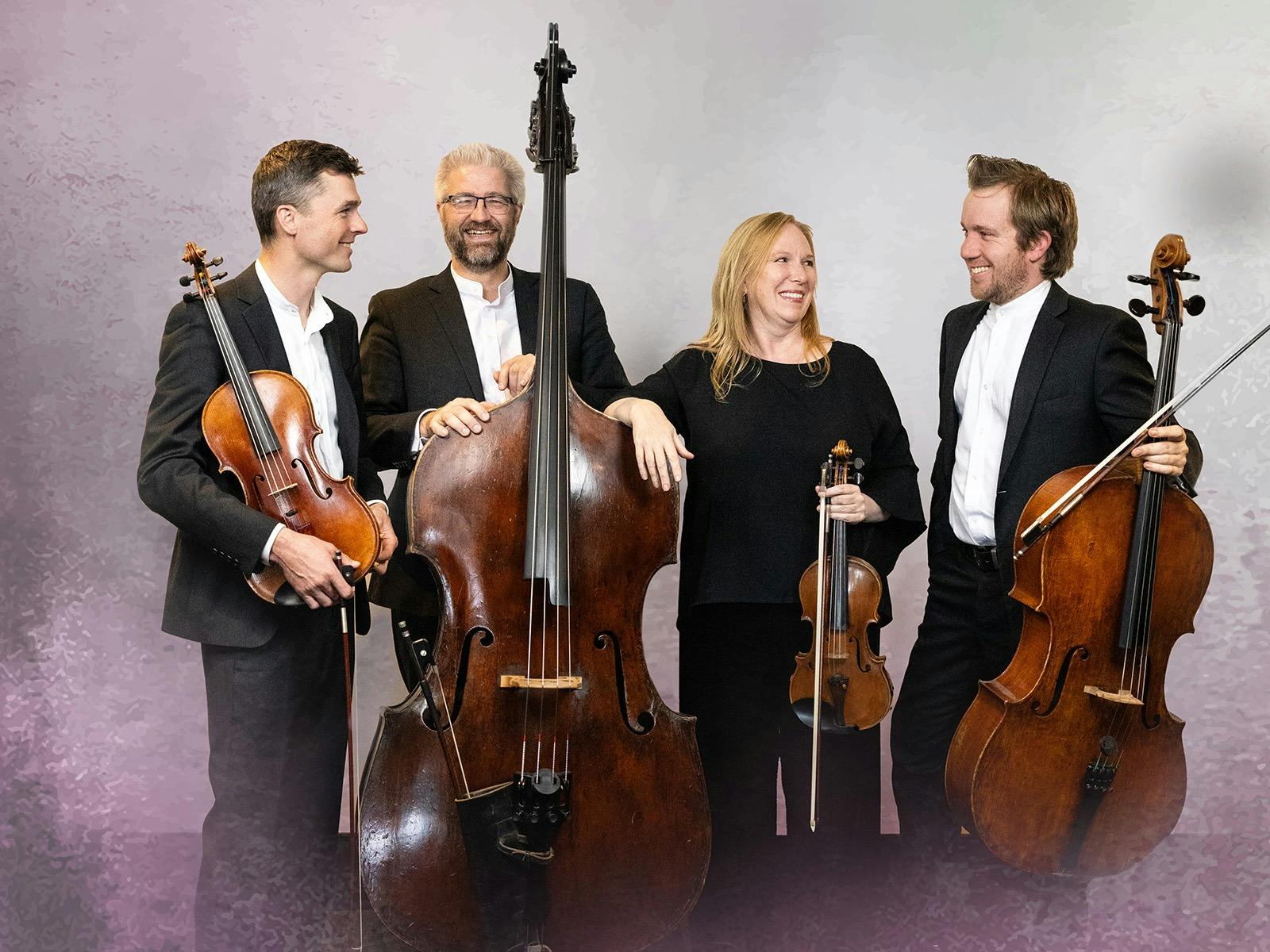 Four musicians pose with their stringed instruments smiling