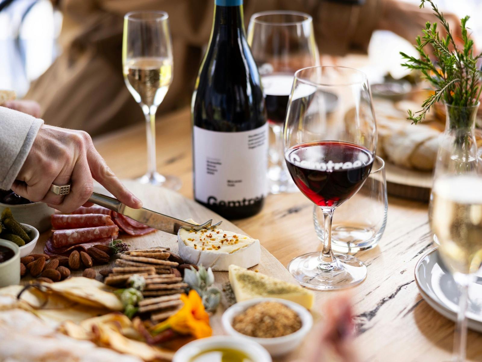 A food platter with a ahdn cutting into cheese, paired with a glass of red wine