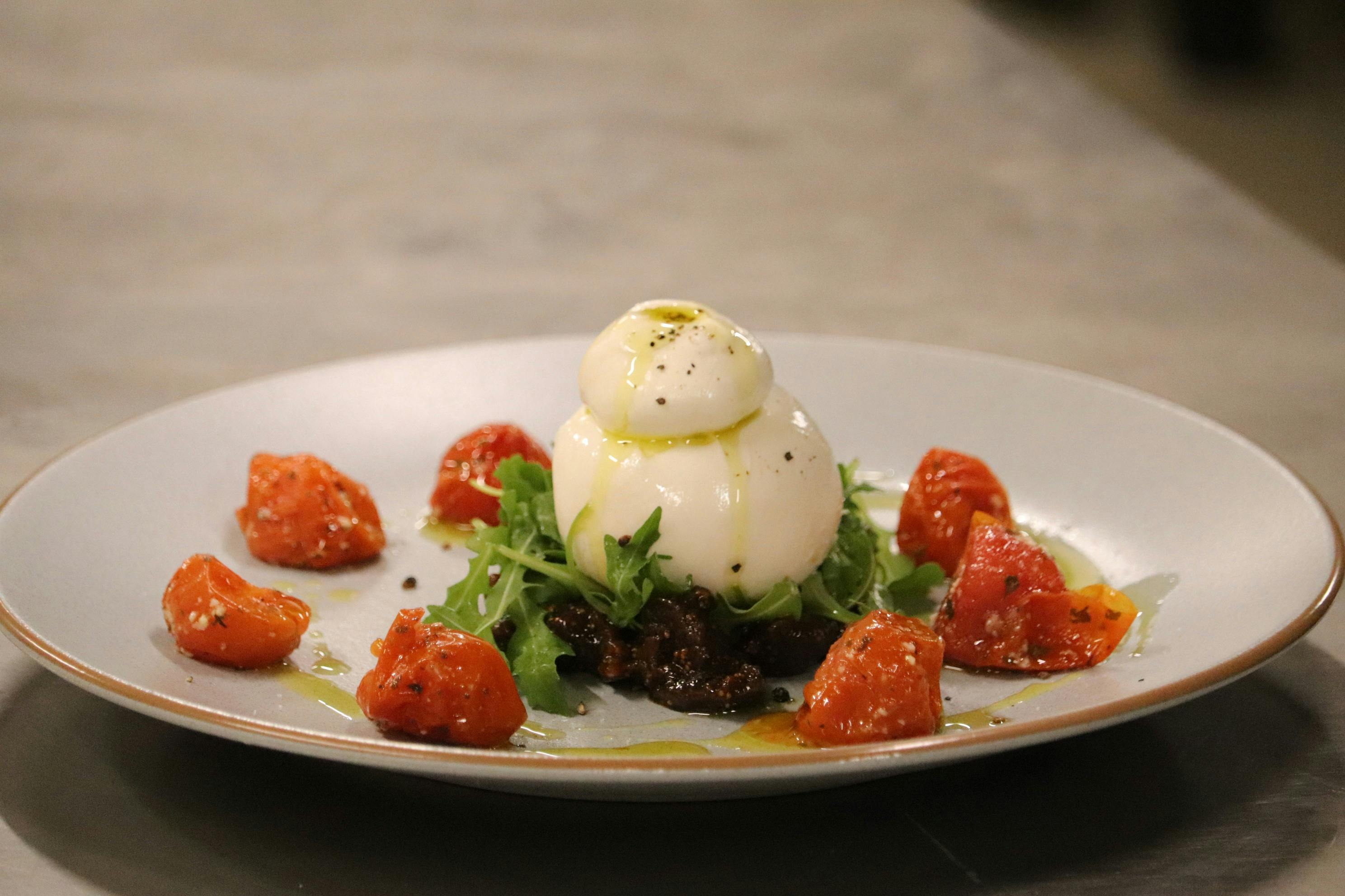 Burrata cheese on greens with roasted cherry tomatoes and olive oil on a white plate.