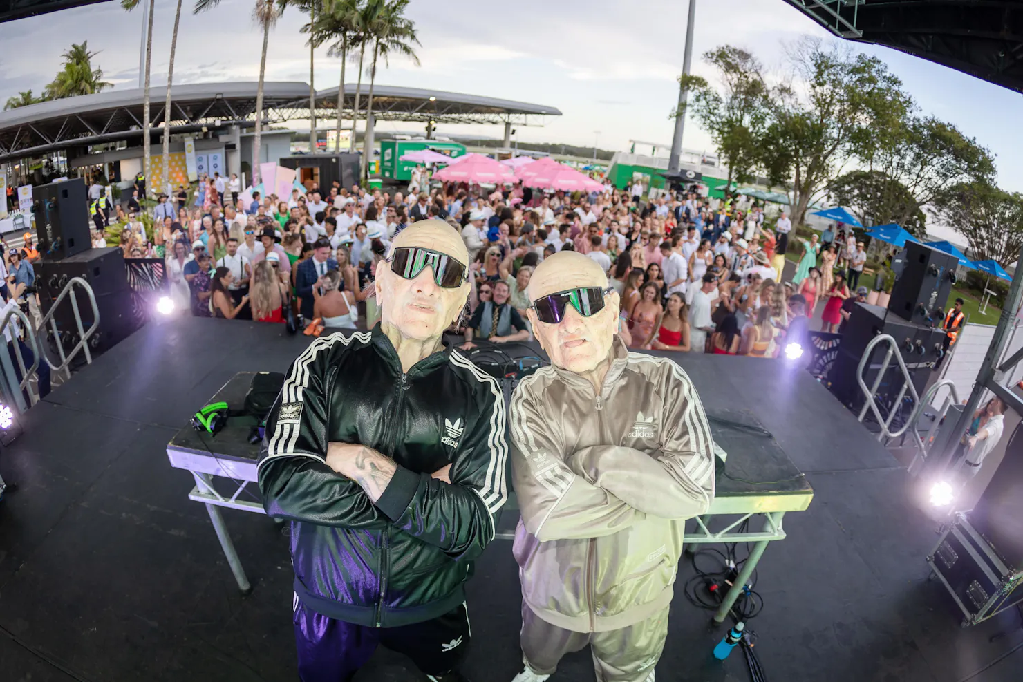 two people dressed as Grandpa DJs on stage with crowd behind them dancing