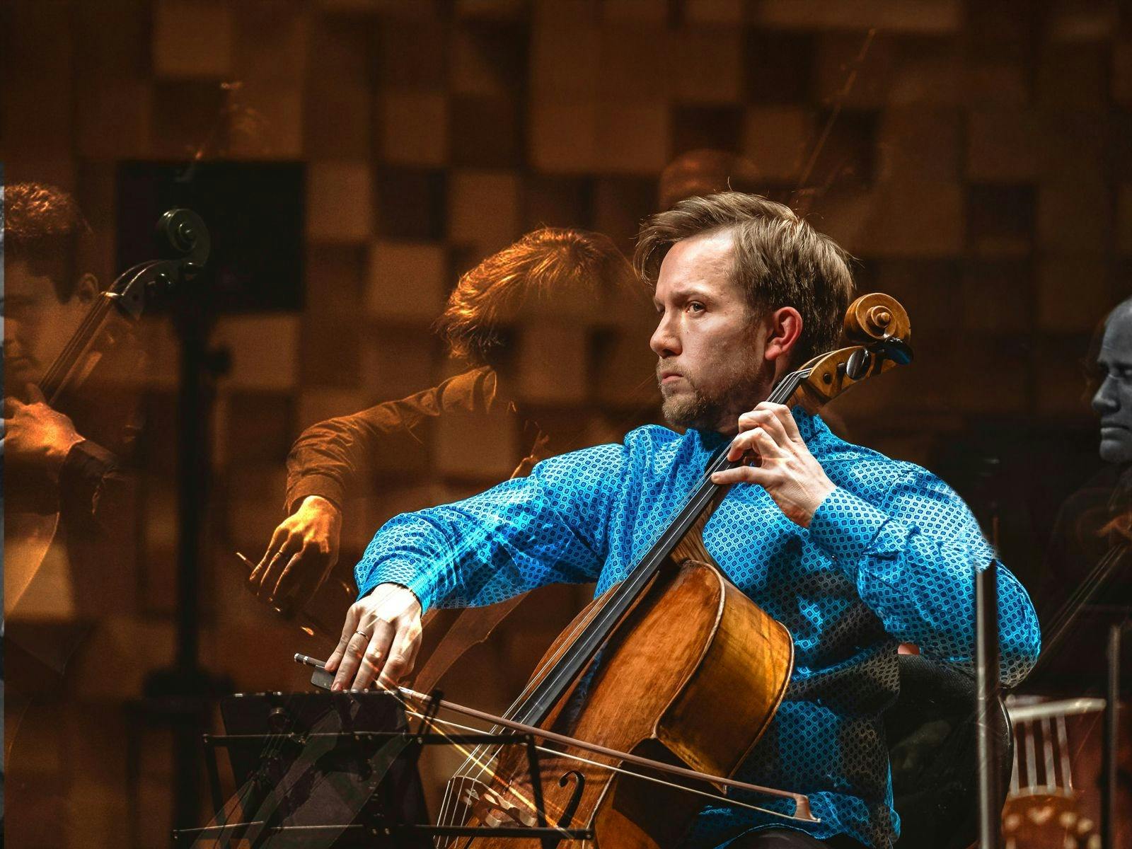 A man in a blue shirt plays a cello on a stage.