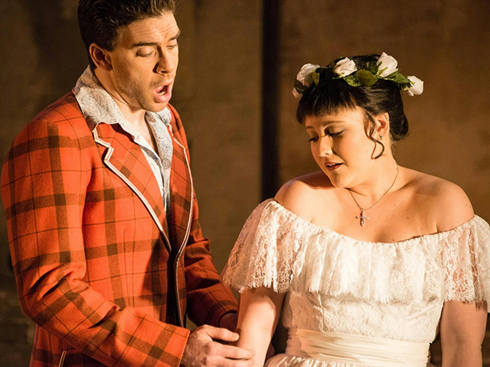 A male and female OPer singer pose mid note, she is dressed in a white lace dress with white roses i