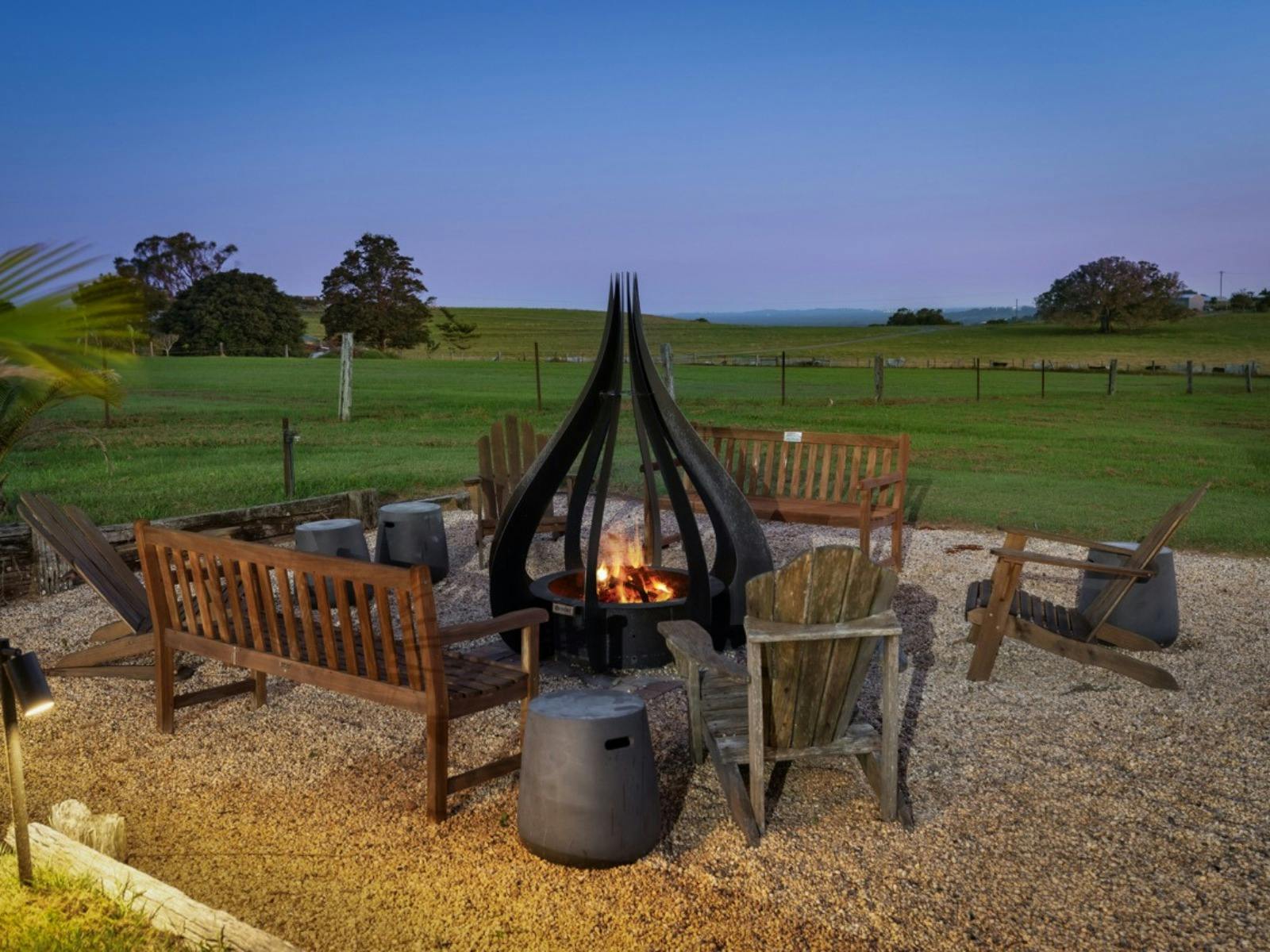 Outdoor fire pit with seating surrounded by expansive rural views at dusk.